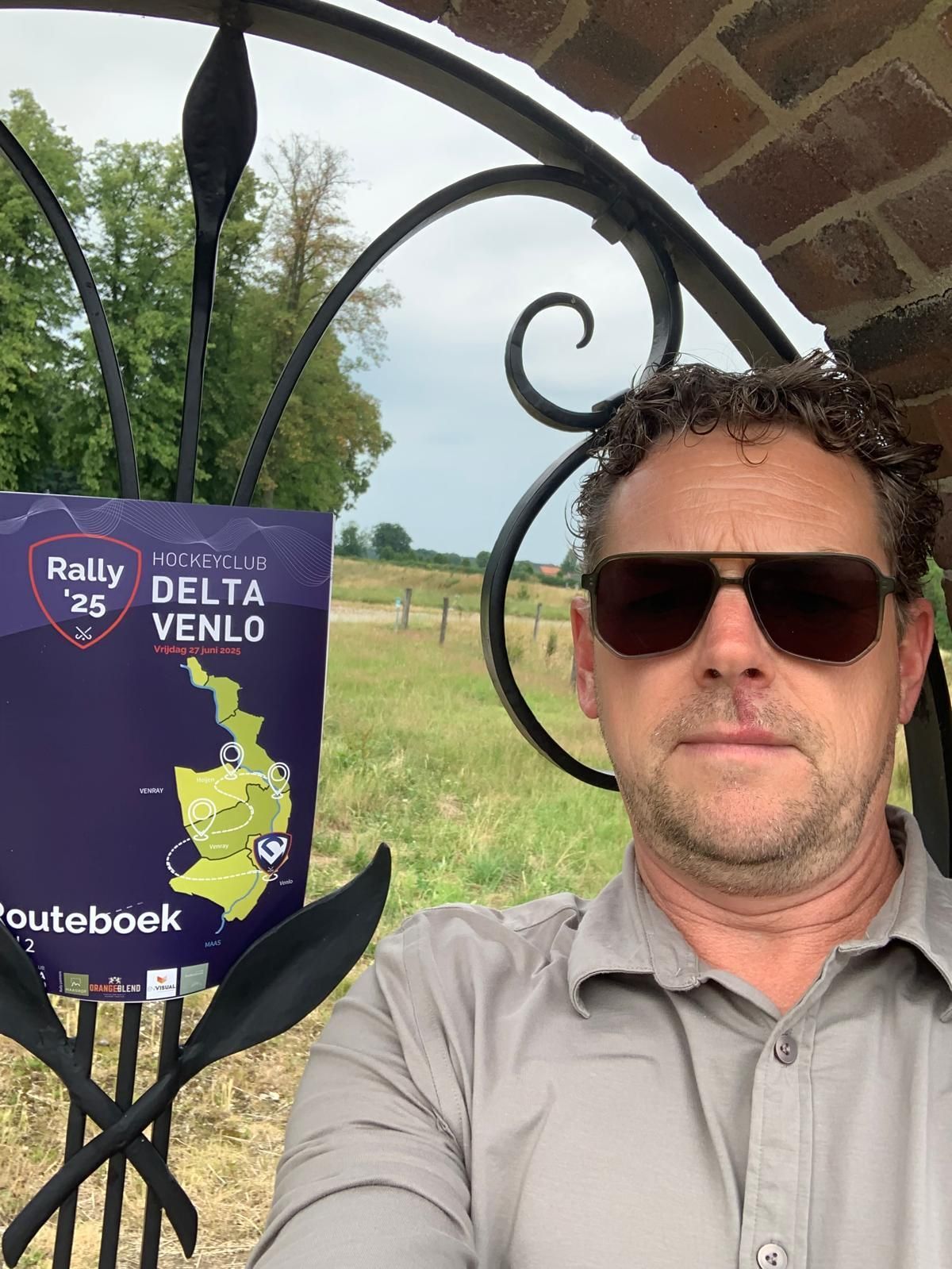 Een man met een zonnebril staat bij een bord met de tekst