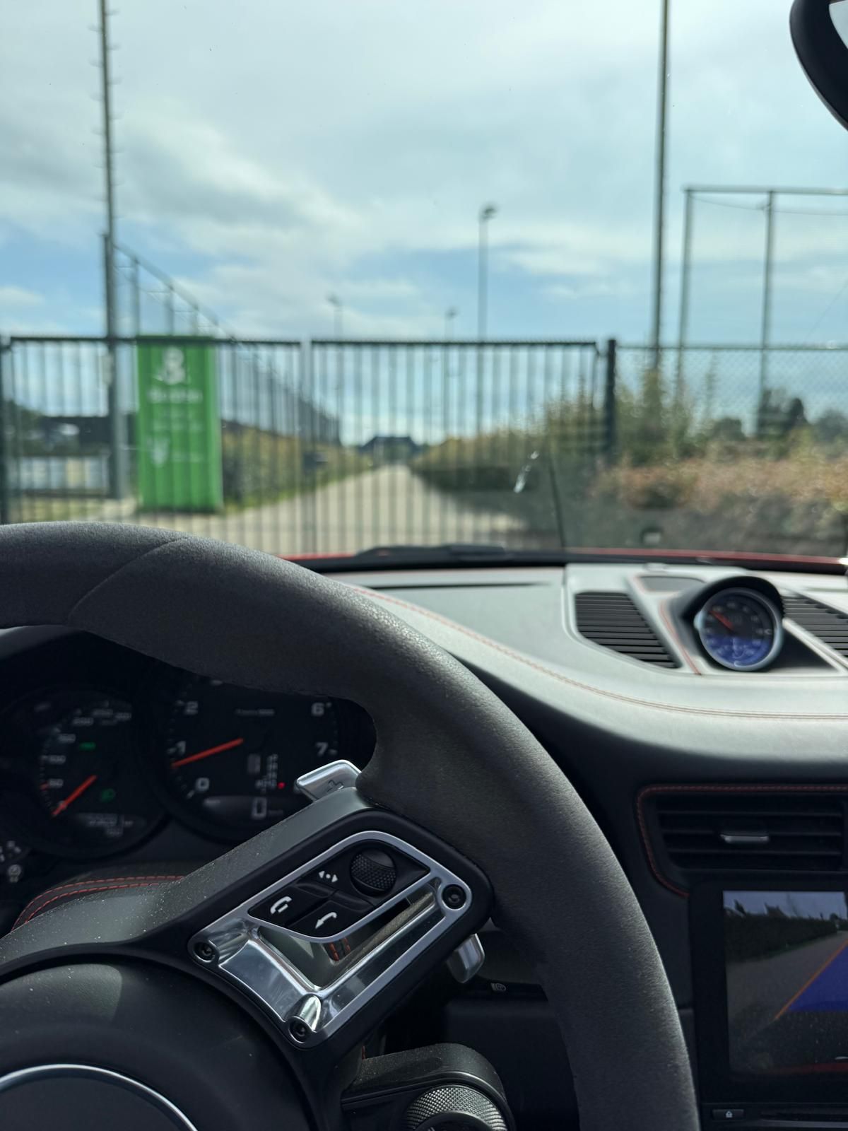 Interieurzicht van een Porsche-stuurwiel; zicht op de poort en de weg ervoor.