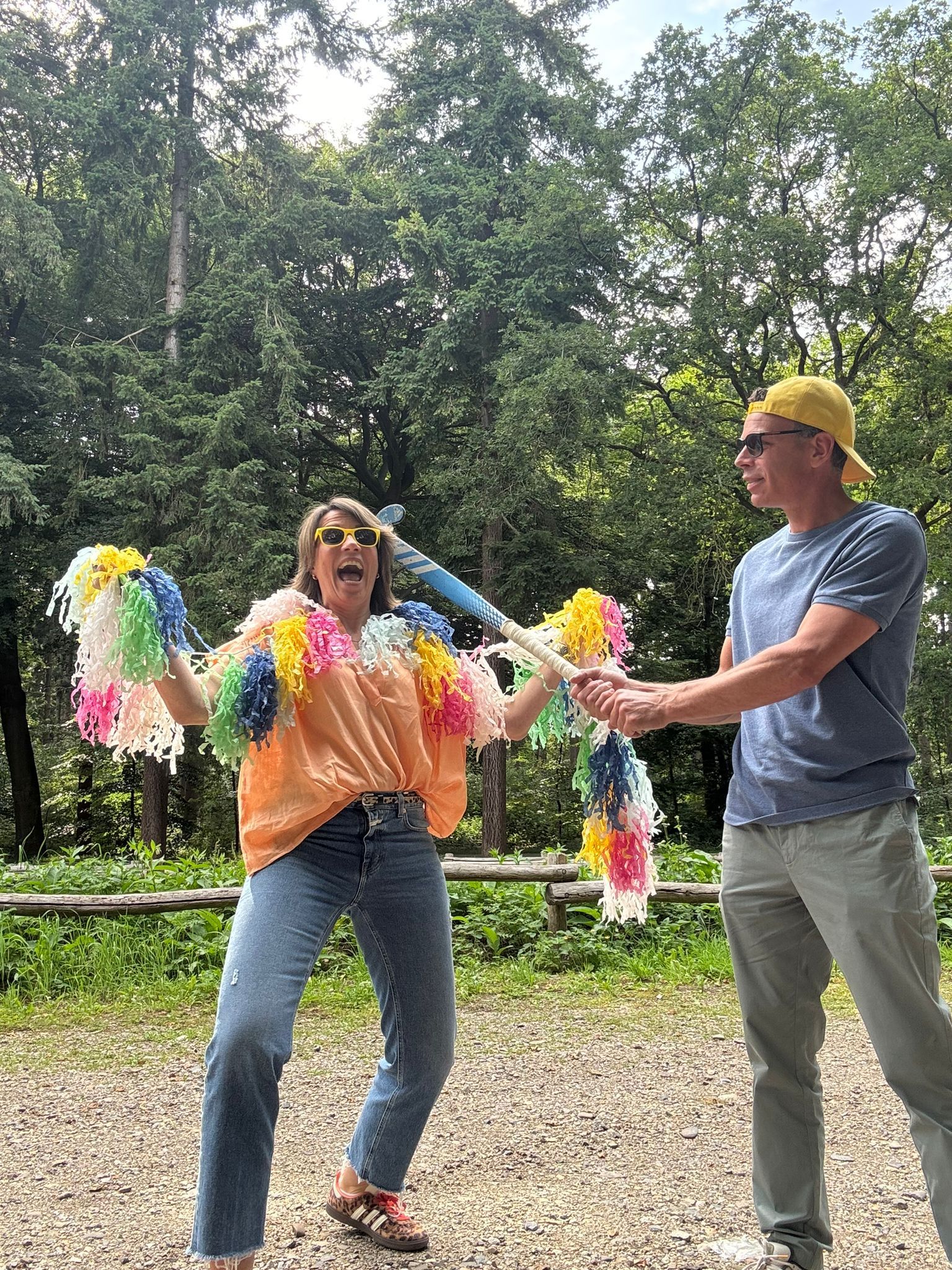 Vrouw met pompons kijkt geschokt, man trekt aan het andere uiteinde. Buiten, omringd door bomen.