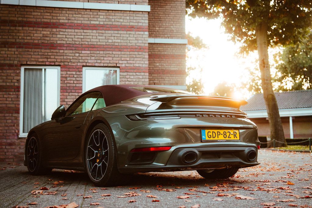 Een donkergroene cabriolet Porsche staat geparkeerd voor een bakstenen gebouw, in het zonlicht.