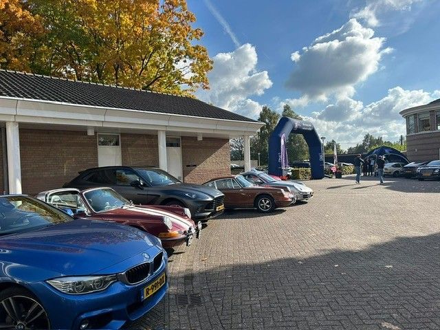 Auto's staan ​​op een rij geparkeerd, waaronder een blauwe BMW, onder een blauwe hemel met een boog op de achtergrond.