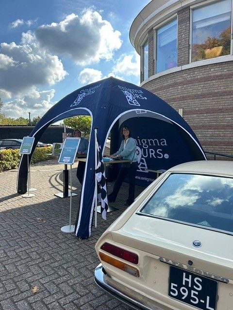 Blauwe luifel voor Enigma Tours met mensen en een klassieke auto ervoor.
