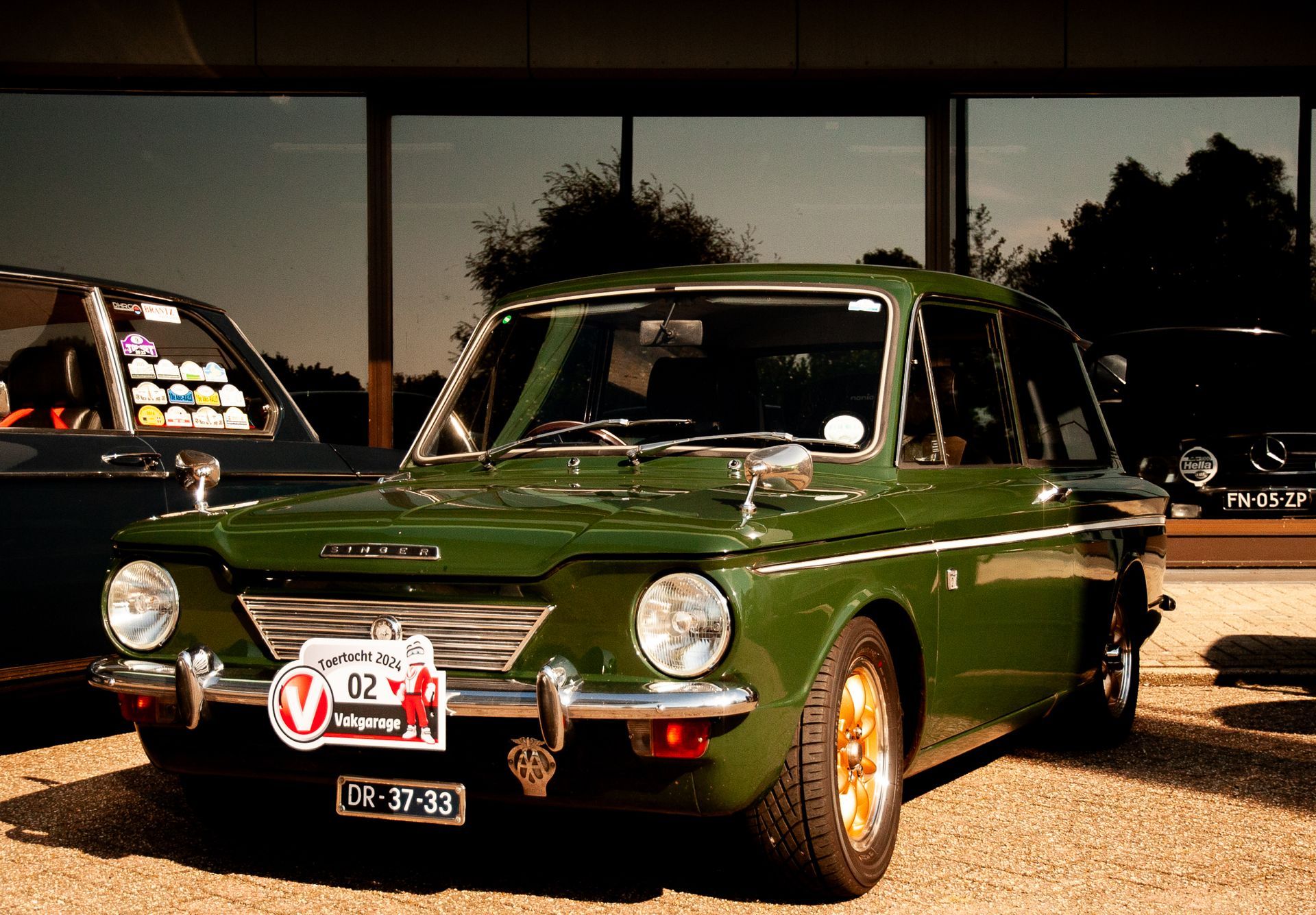 Groene oldtimer geparkeerd voor een gebouw; gouden velgen en witte streep; 
