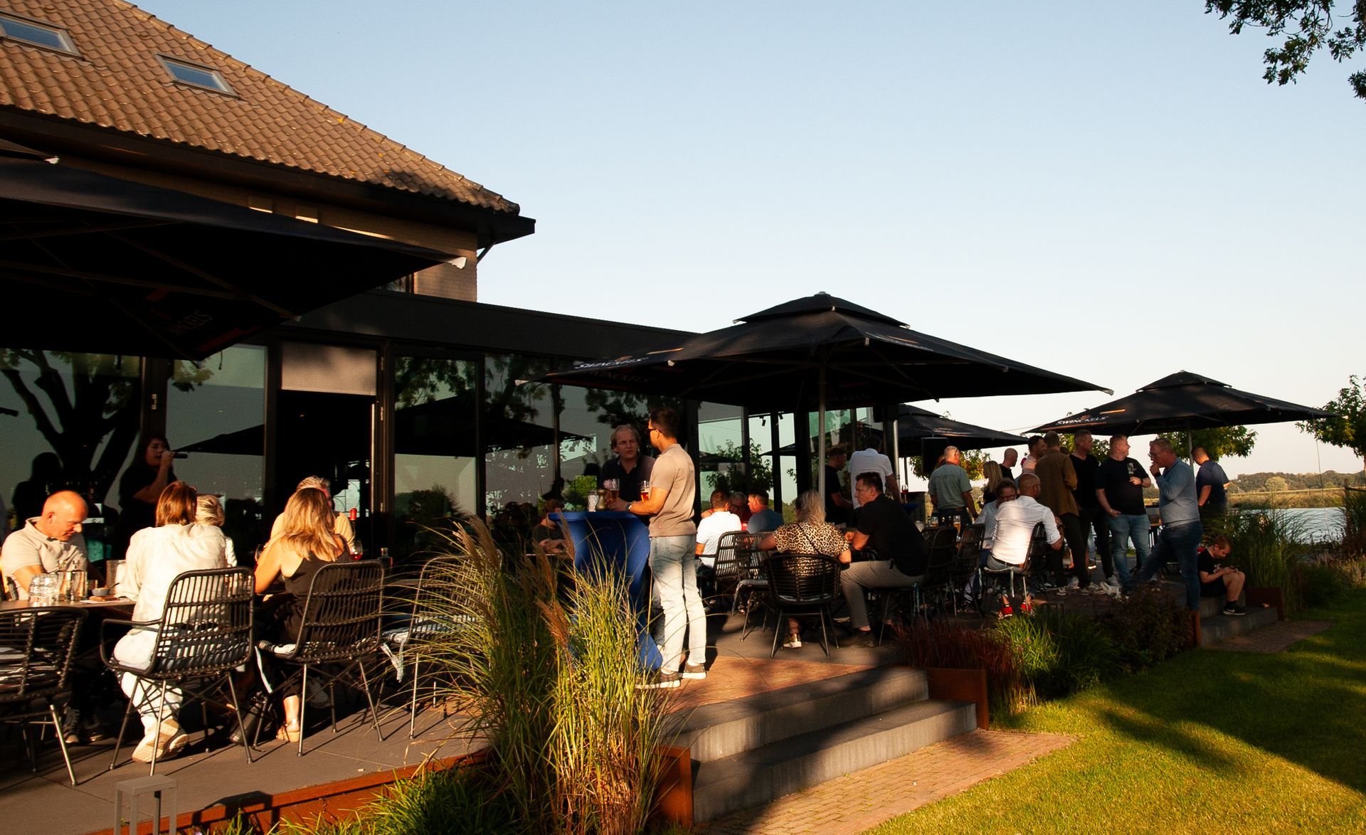 Mensen verzamelen zich op een terras buiten een gebouw met zwarte parasols.