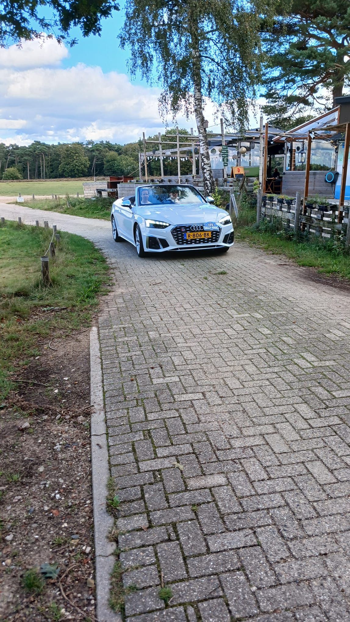 Een witte auto rijdt op een zonnige dag over een bakstenen weg richting hutten.