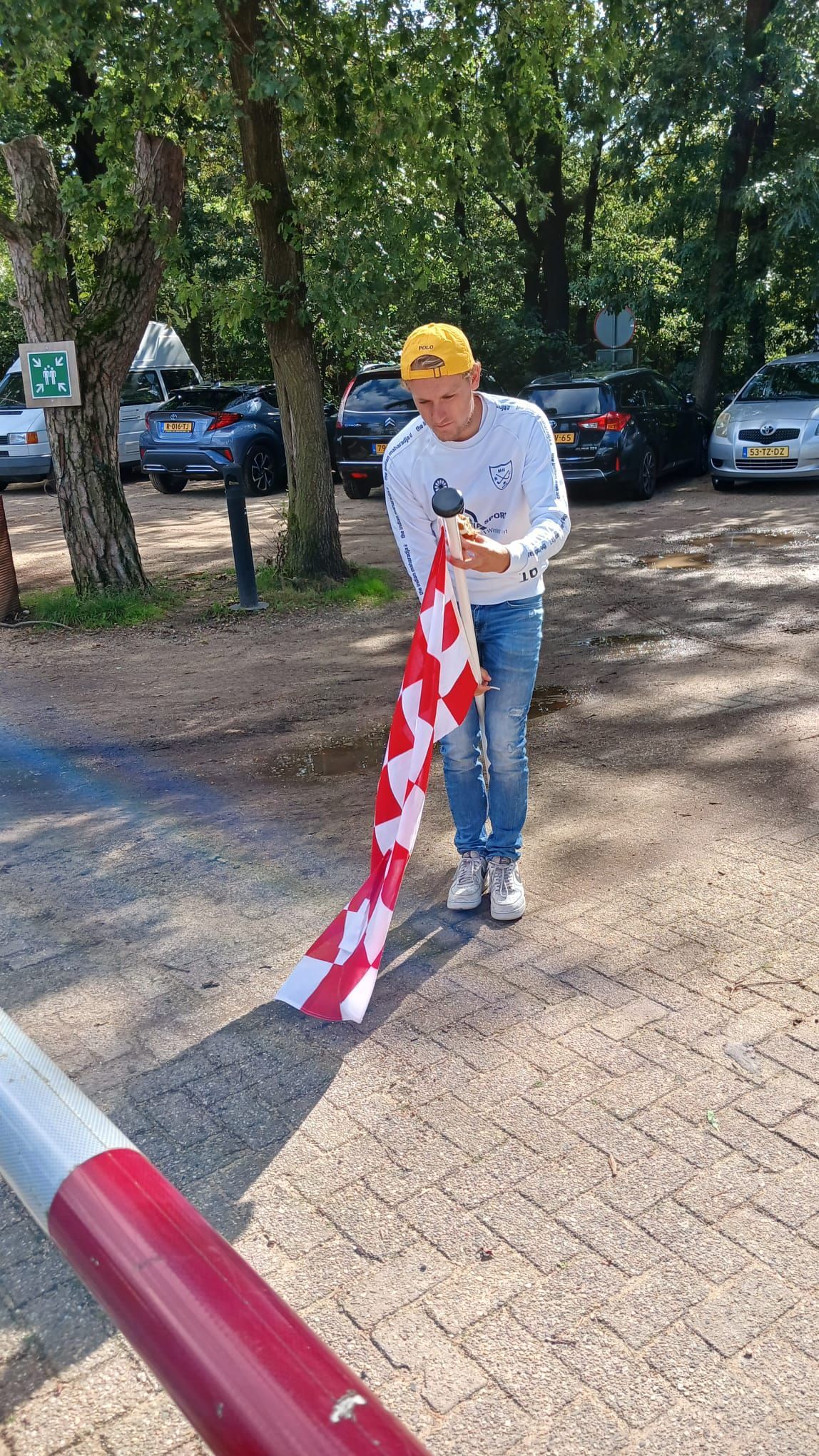 Een man met een rood-wit gestreepte vlag staat bij een parkeerplaats met een slagboom.