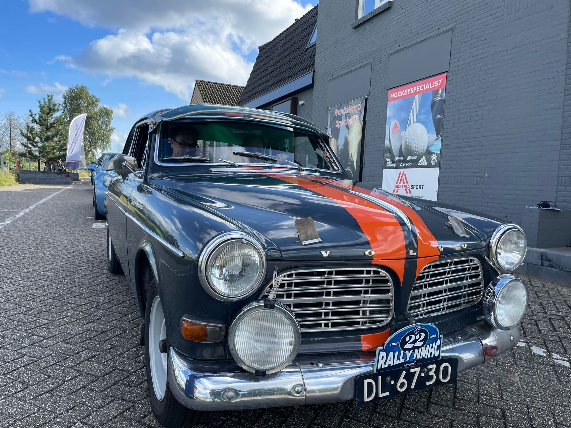 Donkerblauwe vintage Volvo met oranje strepen, geparkeerd bij een gebouw.