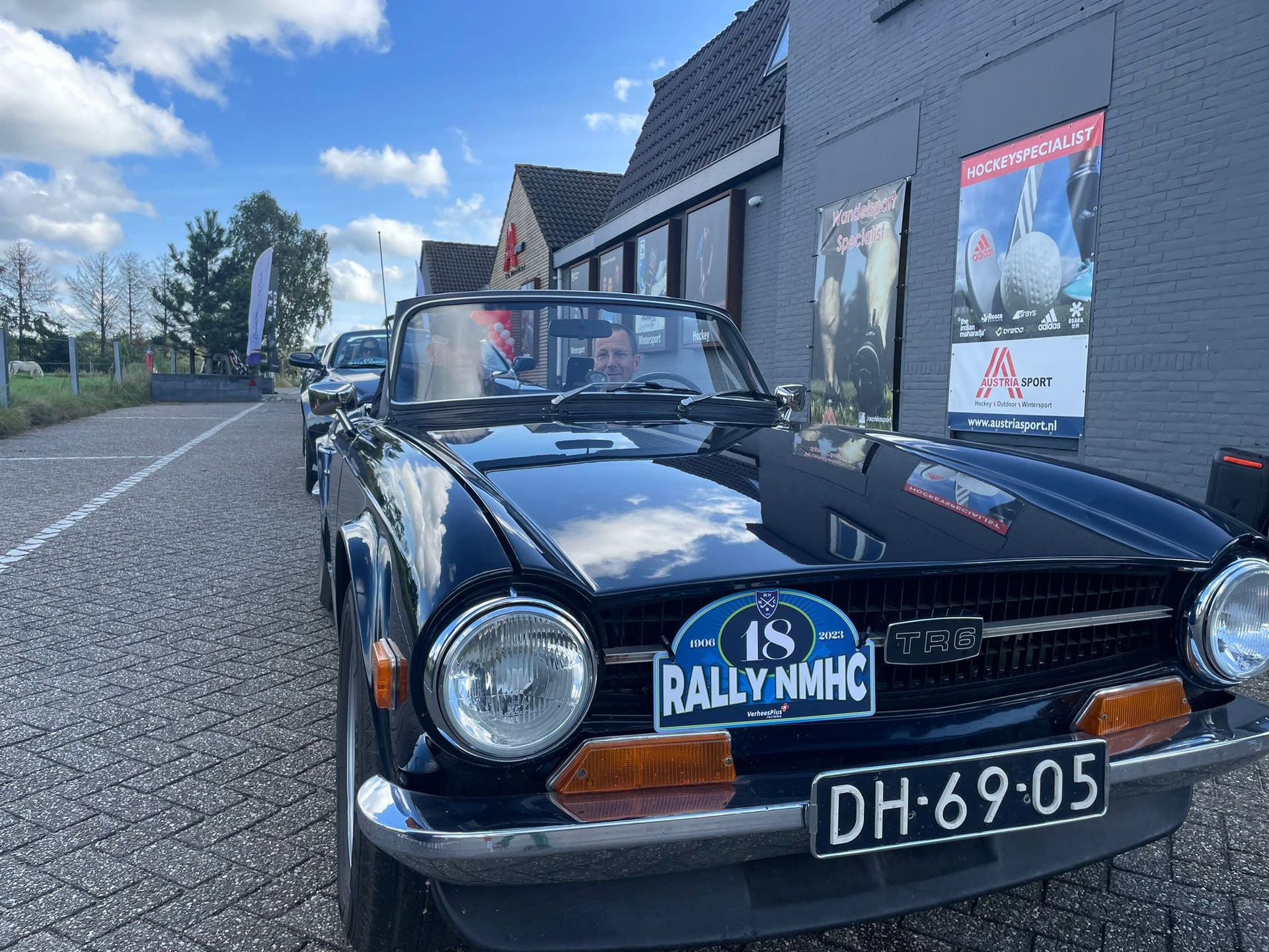 Zwarte cabriolet sportwagen met rally-belettering geparkeerd voor een grijs gebouw.