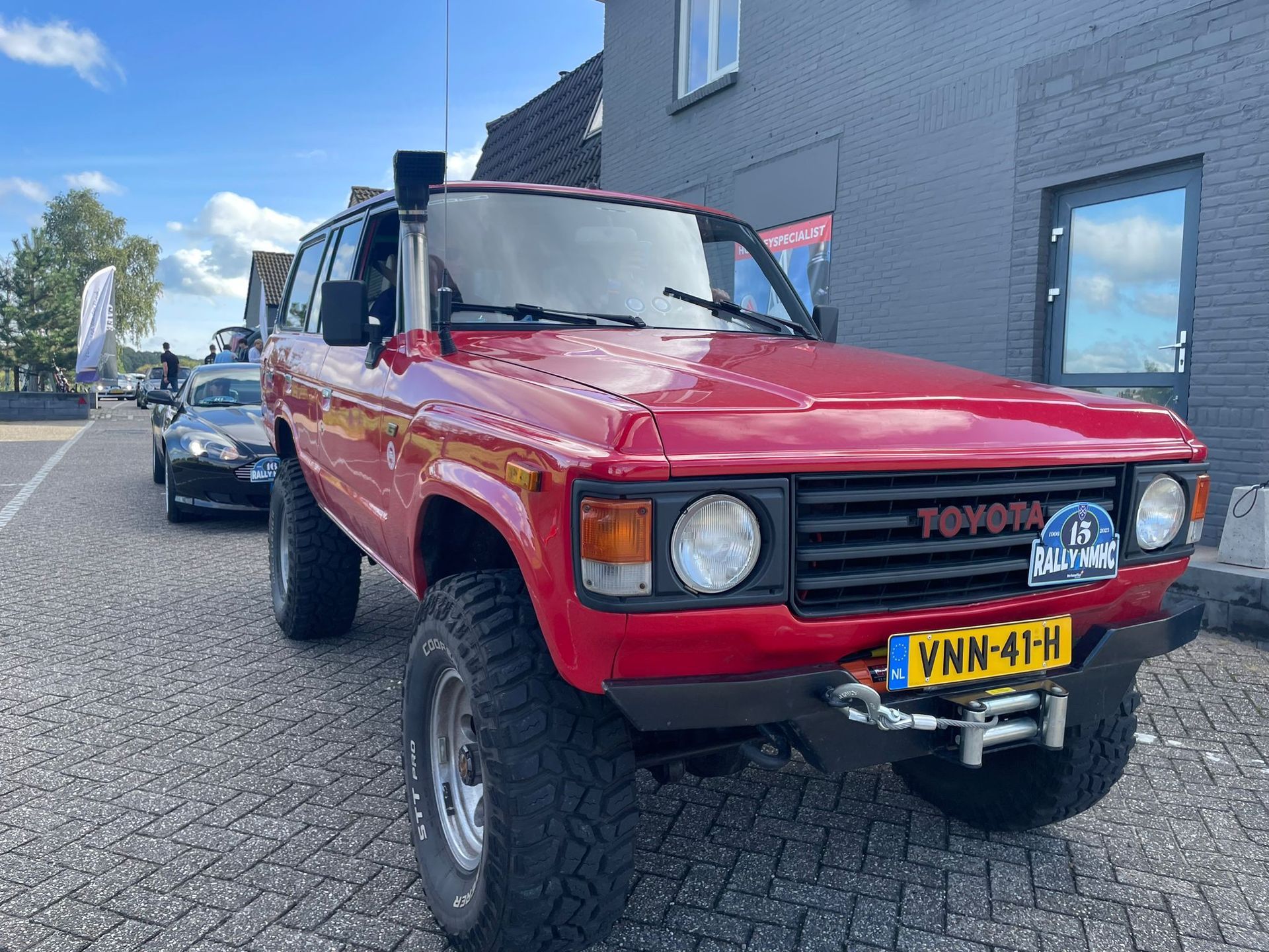Rode Toyota Land Cruiser met snorkel, geparkeerd op een straat met kinderkopjes.