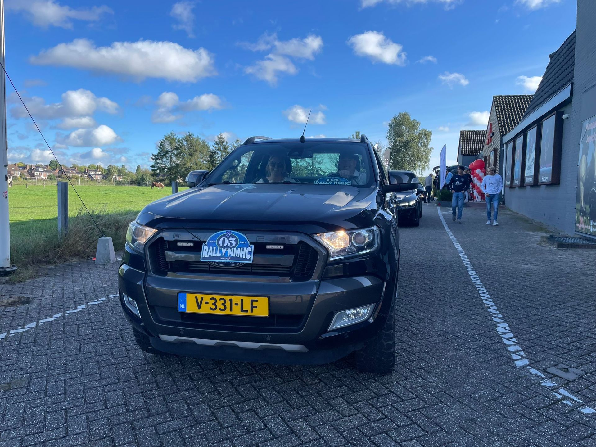 Donkergrijze Ford Ranger met Nederlands kenteken, geparkeerd op een straat met kinderkopjes. Mensen lopen ernaast.