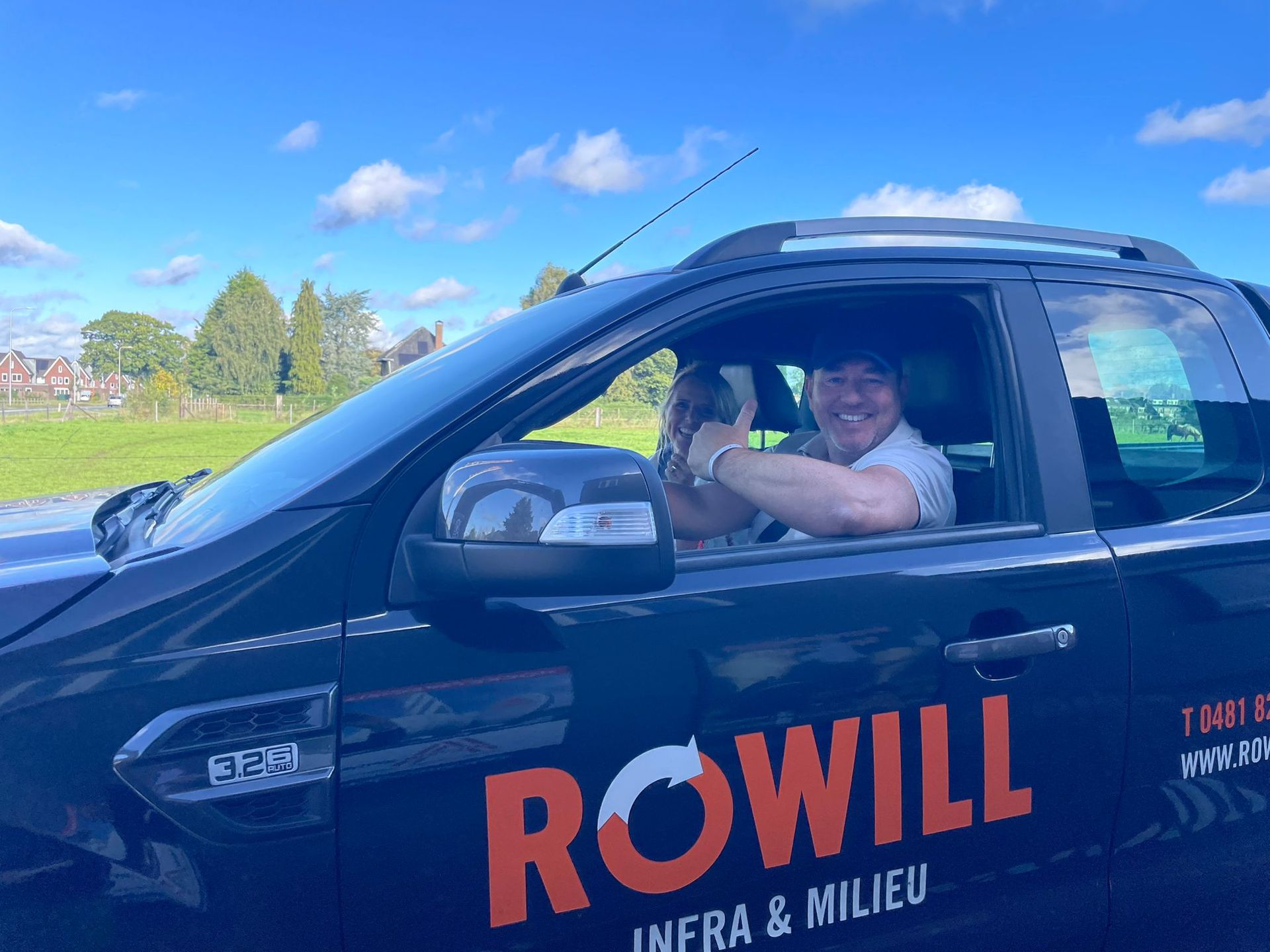 Man in een donkere pick-up truck, glimlachend met de armen over elkaar. 