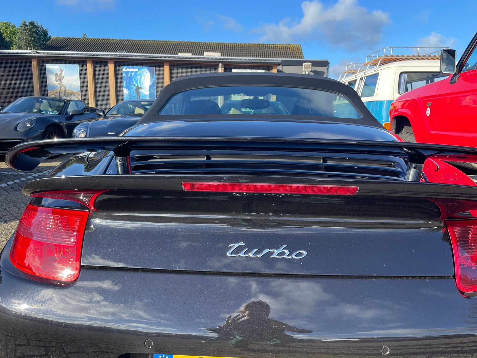 Zwarte Porsche 911 Turbo cabriolet met spoiler, geparkeerd tussen andere voertuigen.