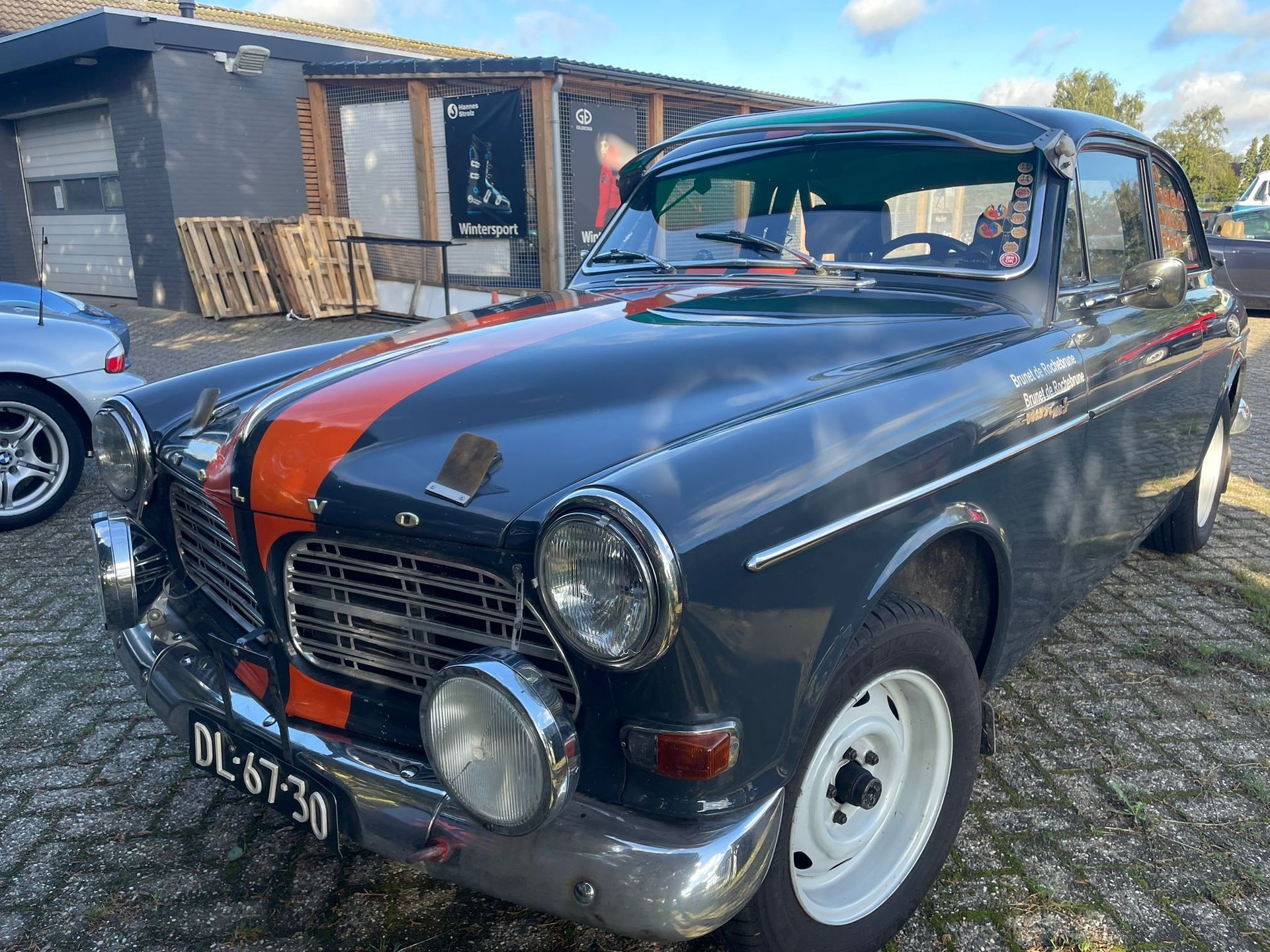 Donkerblauwe vintage Volvo met oranje streep, witte velgen en schijnwerpers, buiten geparkeerd.