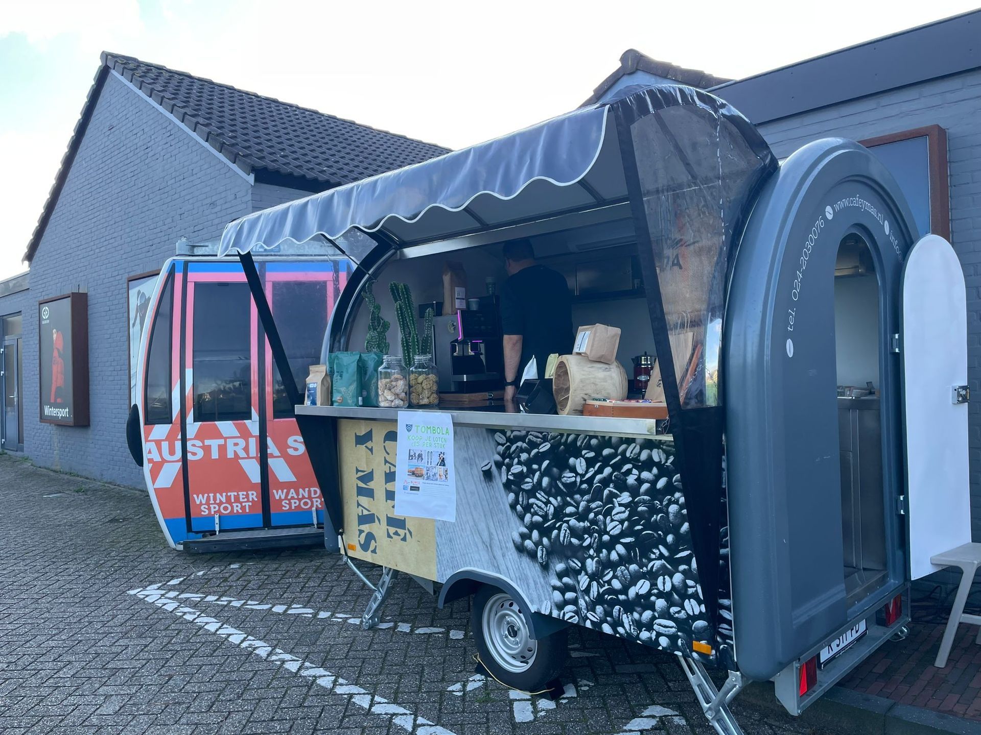 Twee foodtrucks staan ​​geparkeerd naast een bakstenen gebouw. ​​Op de ene staat 