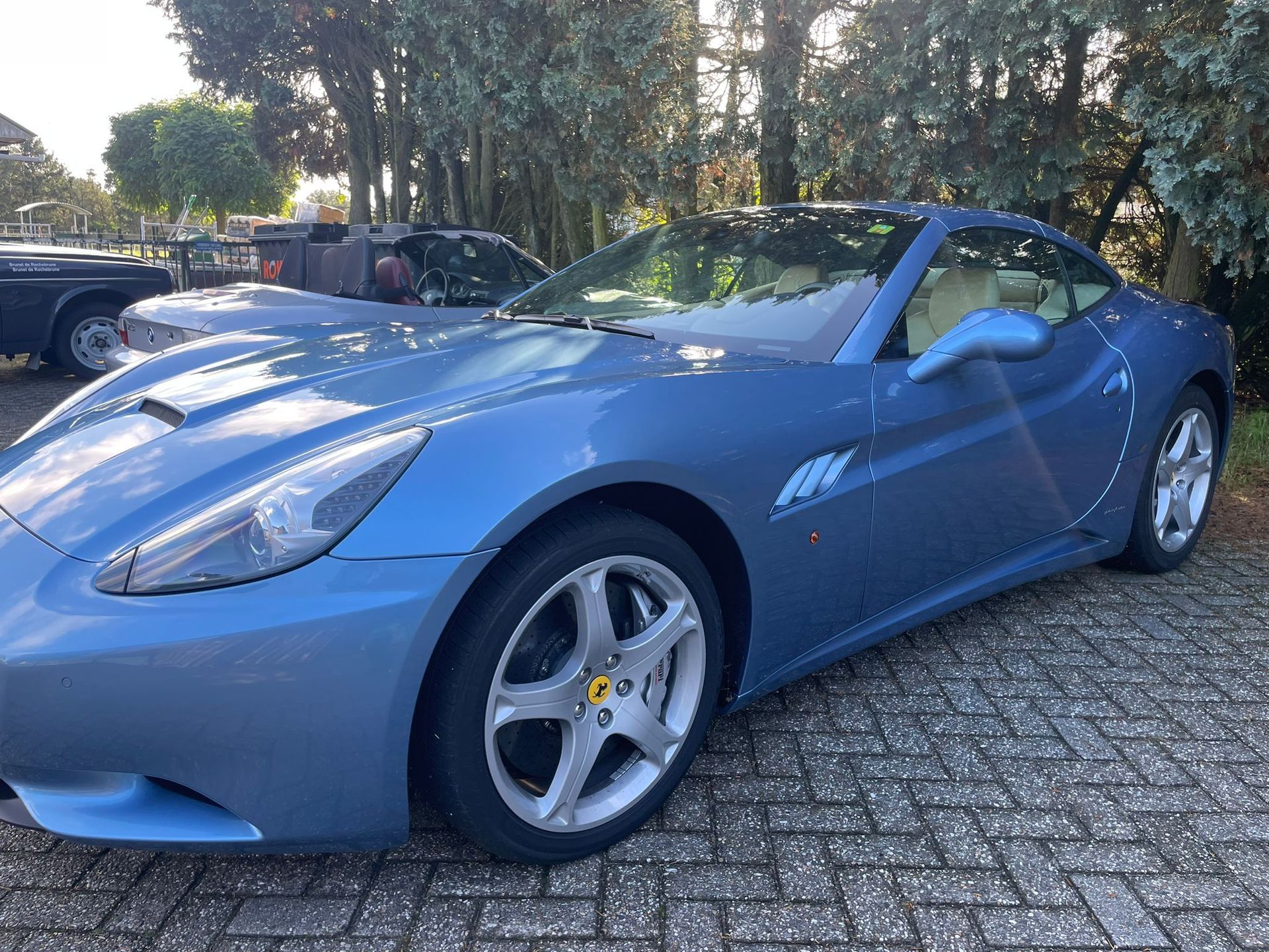 Blauwe Ferrari California geparkeerd op een bestrating van bakstenen.