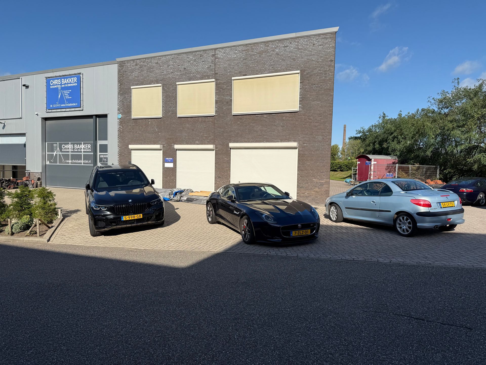 Auto's geparkeerd voor een gebouw met garagedeuren. Zonlicht op een blauwe hemel.