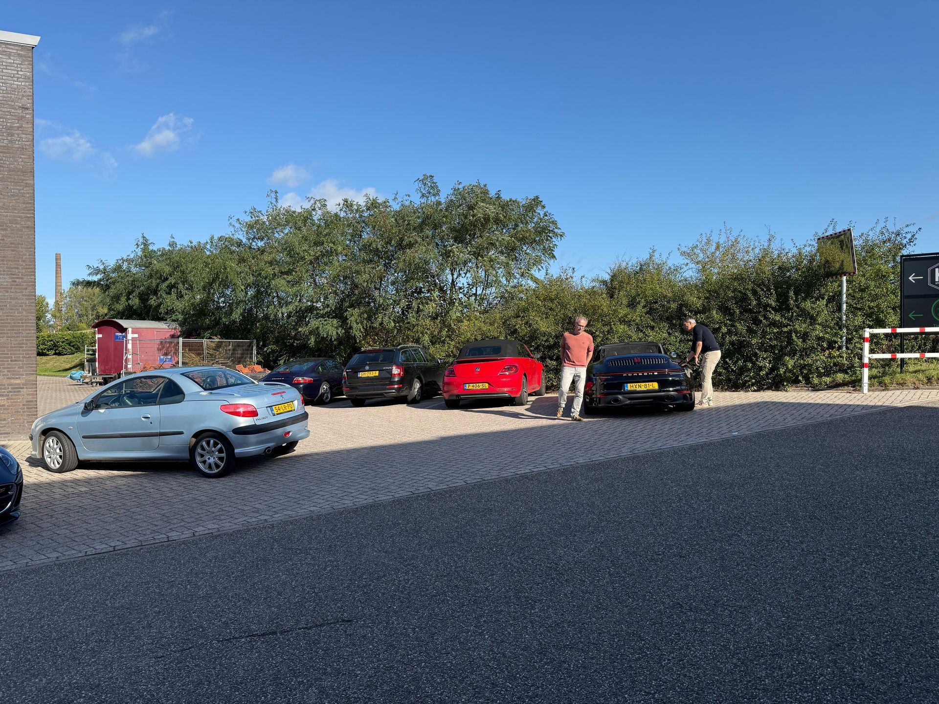 Er stonden meerdere auto's geparkeerd op een grindpad, met twee mensen die eronder stonden onder een blauwe hemel.