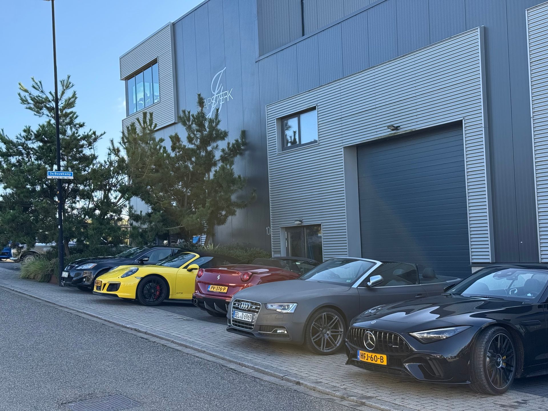 Een rij sportauto's geparkeerd voor een modern gebouw met een donkergrijze gevel.