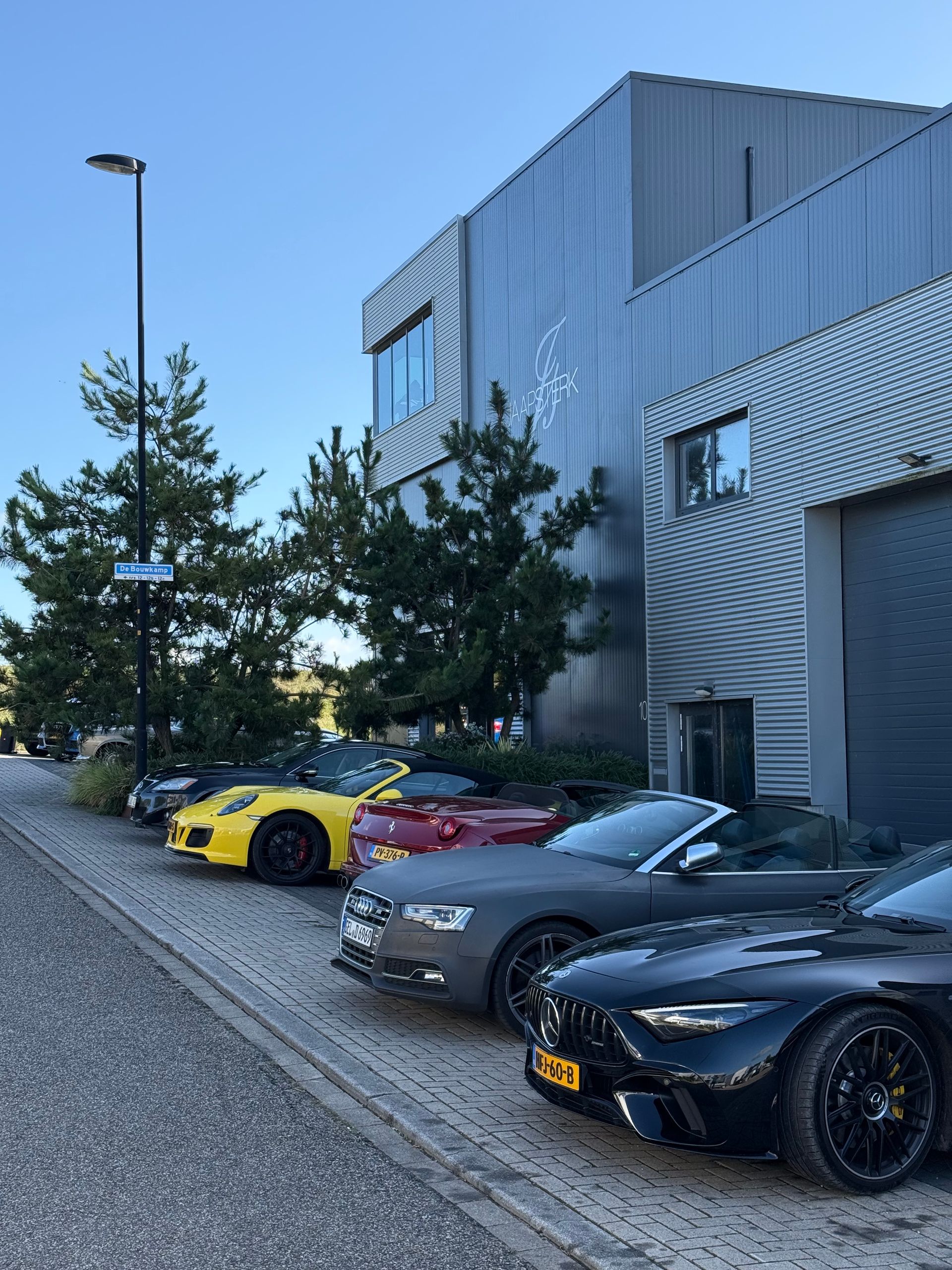 Luxe auto's geparkeerd voor een modern gebouw. Zwarte, gele en rode cabriolets zijn zichtbaar.