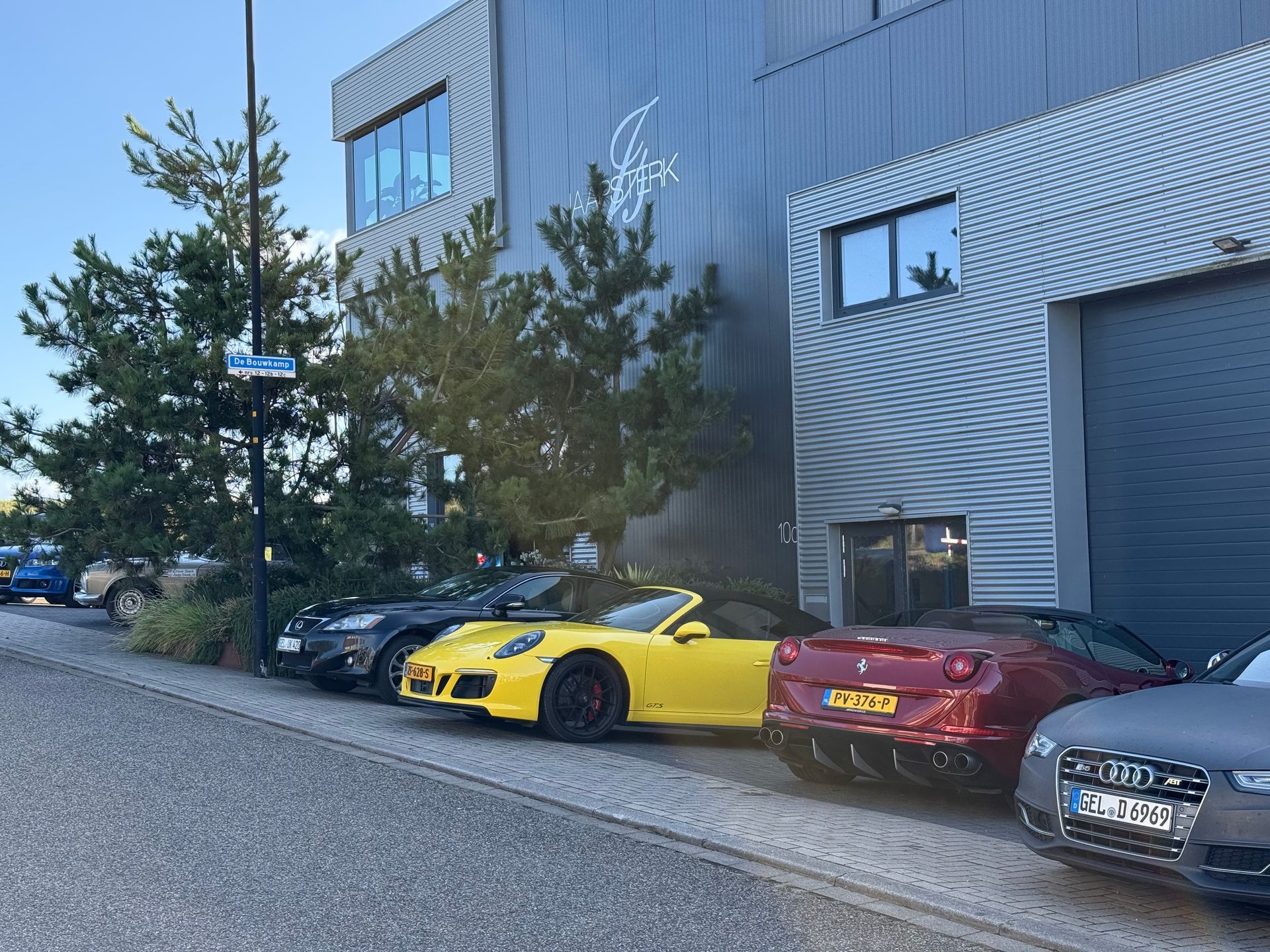 Auto's geparkeerd voor een modern gebouw. Onder andere een gele cabriolet, een rode auto en een grijze auto.