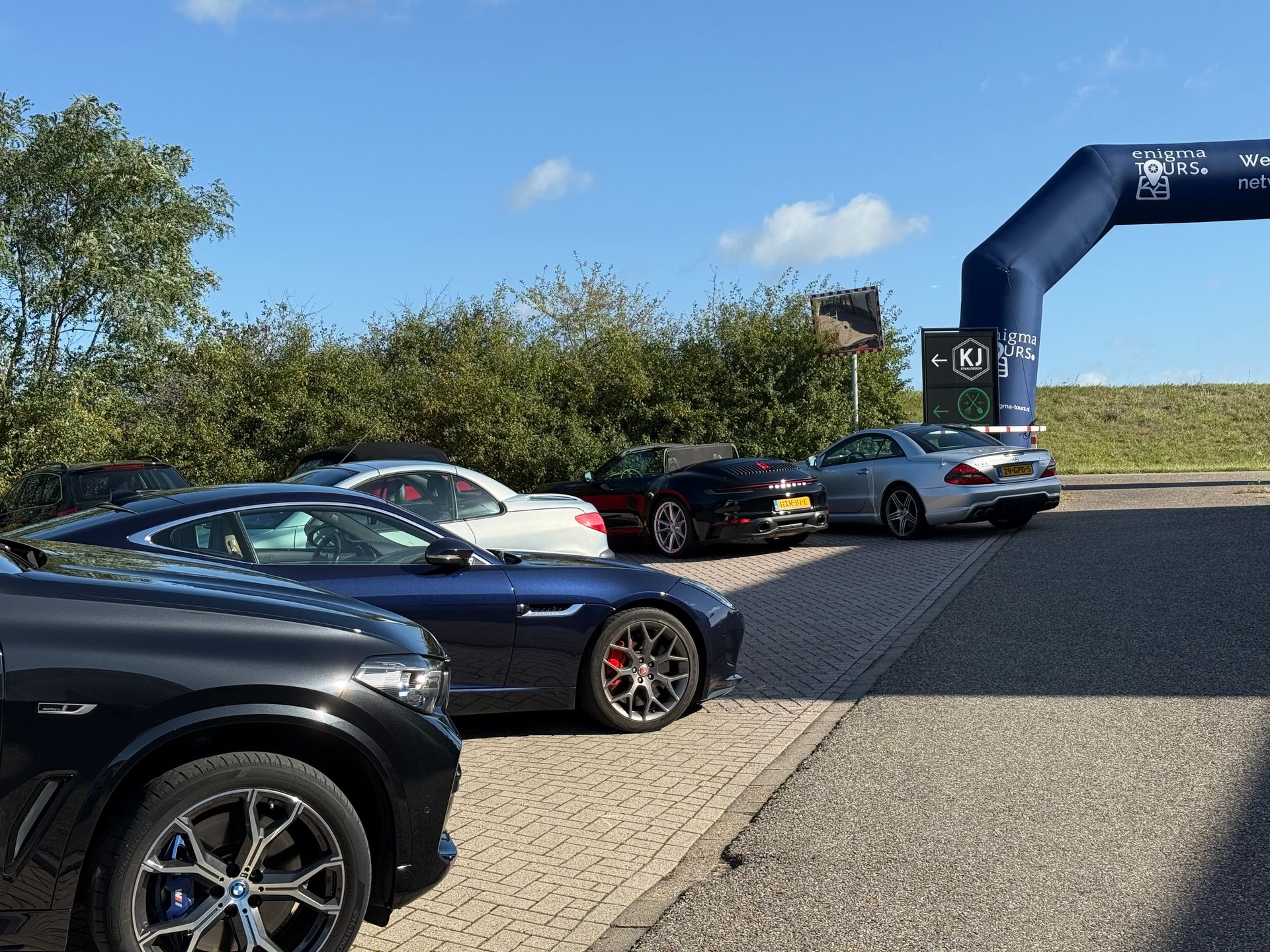 Auto's geparkeerd bij een poort; een zwarte BMW op de voorgrond, andere sportwagens in verschillende kleuren.
