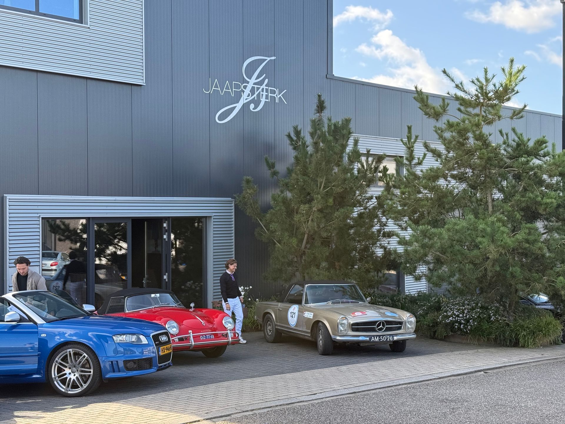 Auto's geparkeerd voor een gebouw met mensen in de buurt. Klassieke rode en gouden auto's, een blauwe sportwagen.