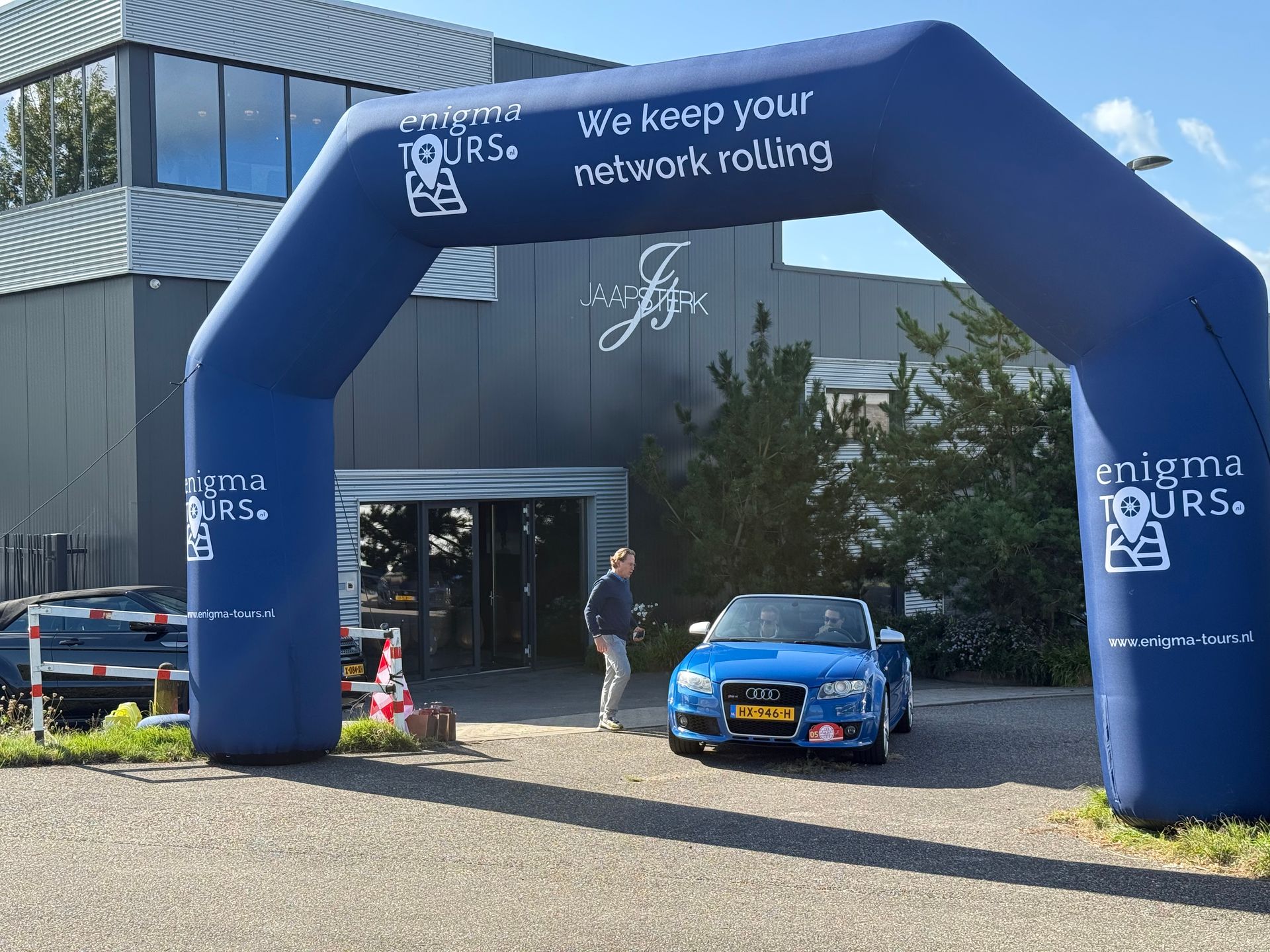 Een blauwe auto rijdt onder een opblaasbare boog door met reclame voor