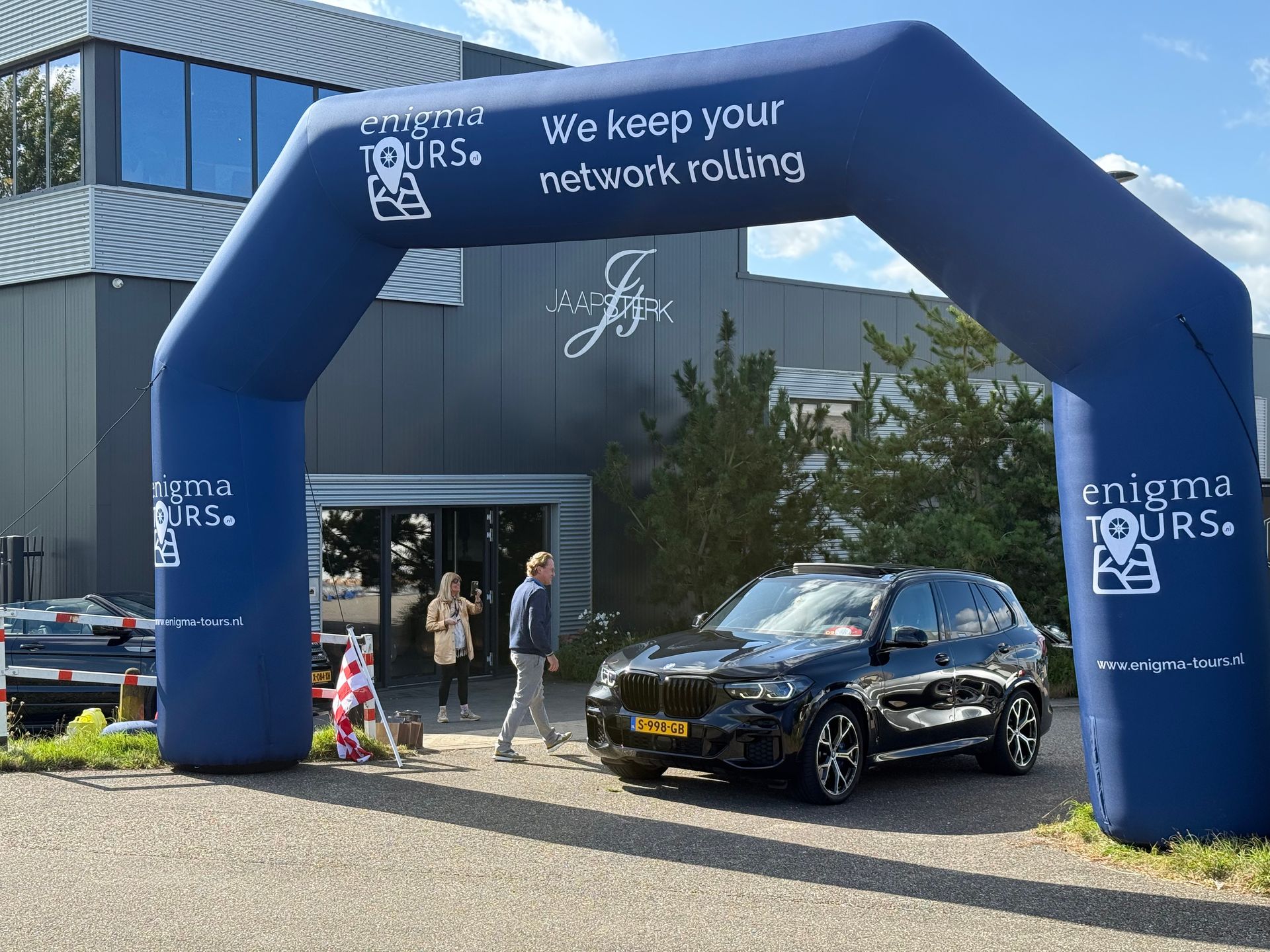 Een zwarte SUV staat onder een blauwe opblaasbare boog met de tekst