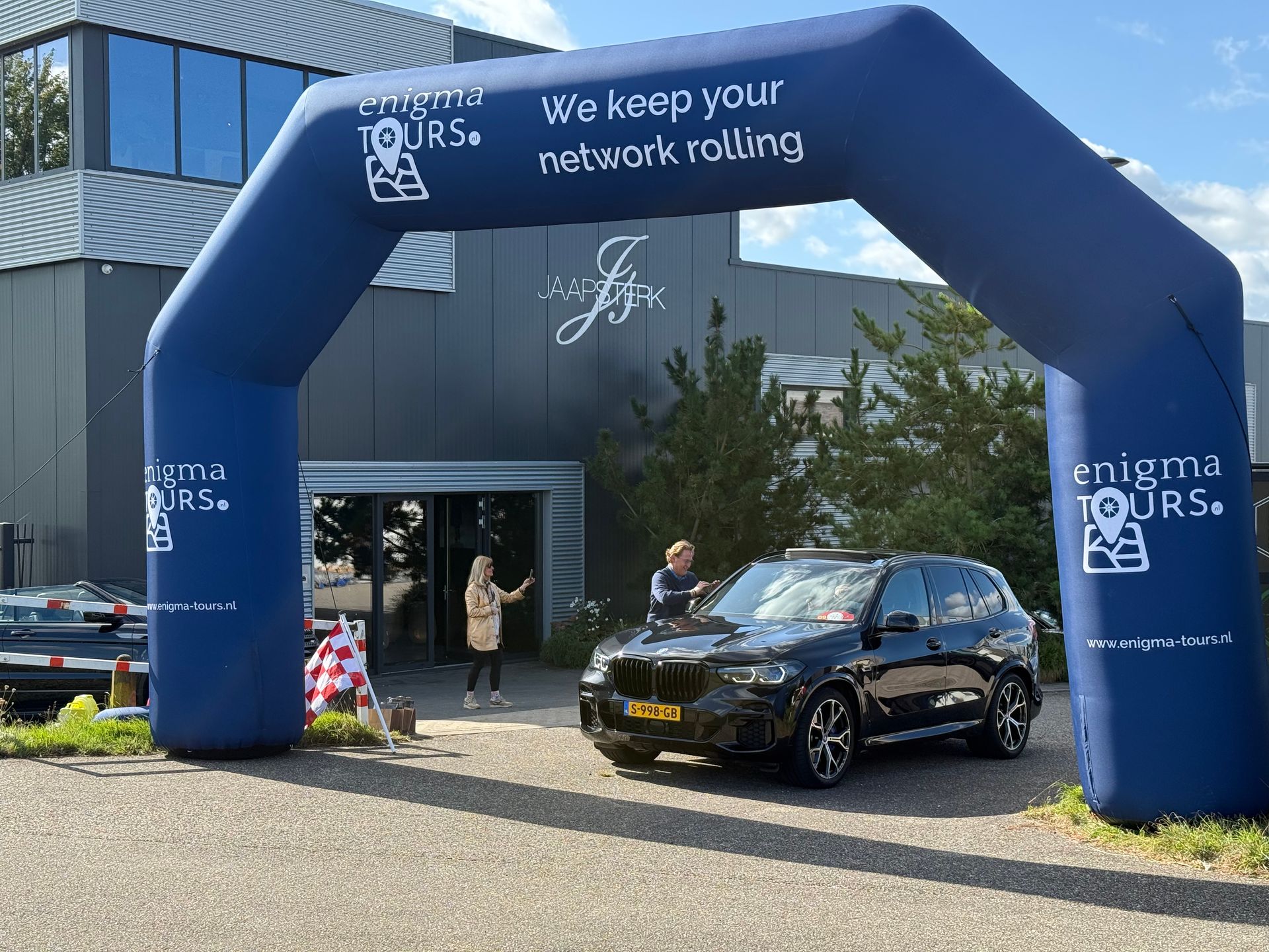Een zwarte SUV staat geparkeerd onder een opblaasbare boog met het opschrift