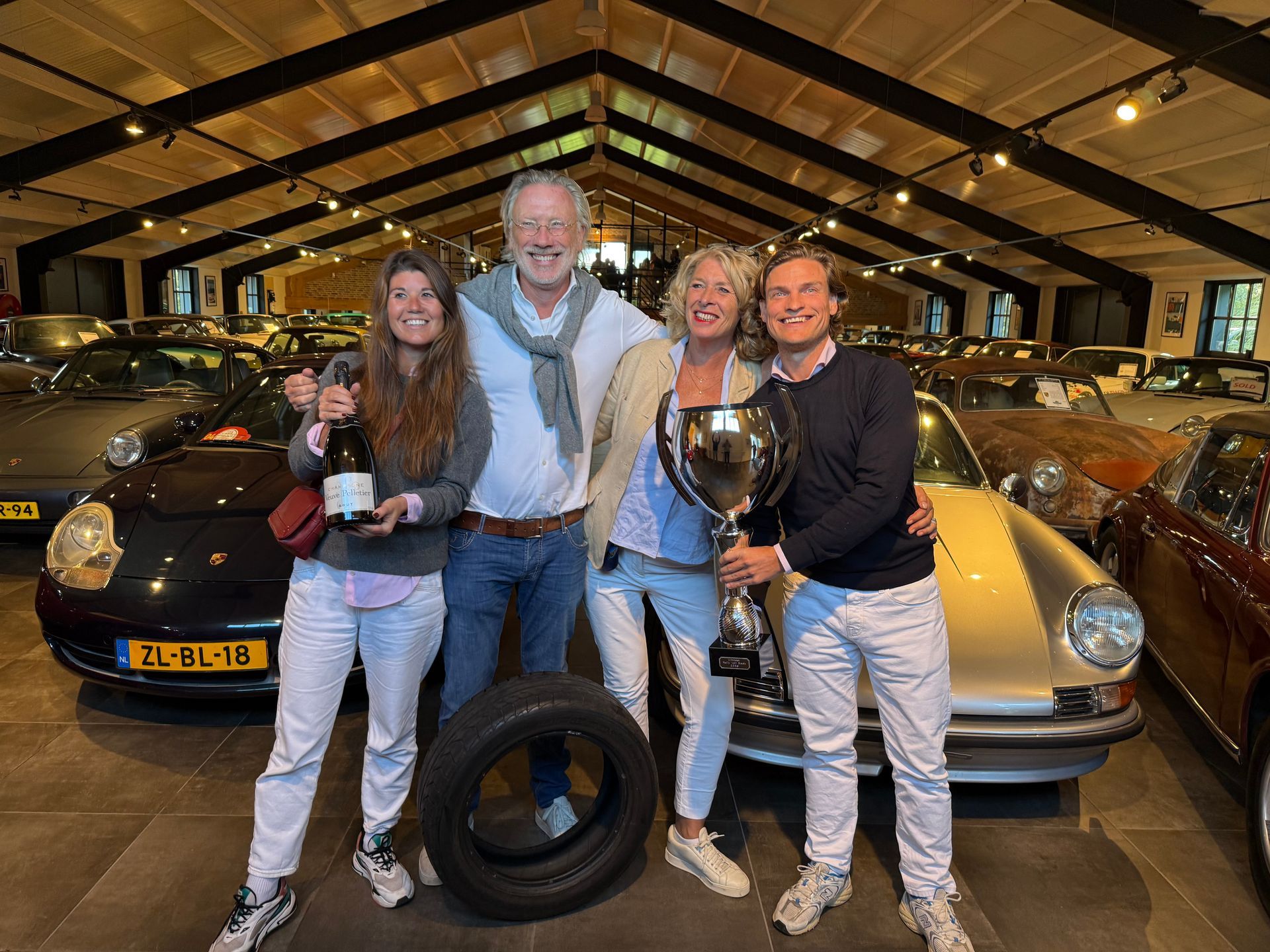 Een groep mensen viert feest met een trofee en champagne in een autoshowroom.