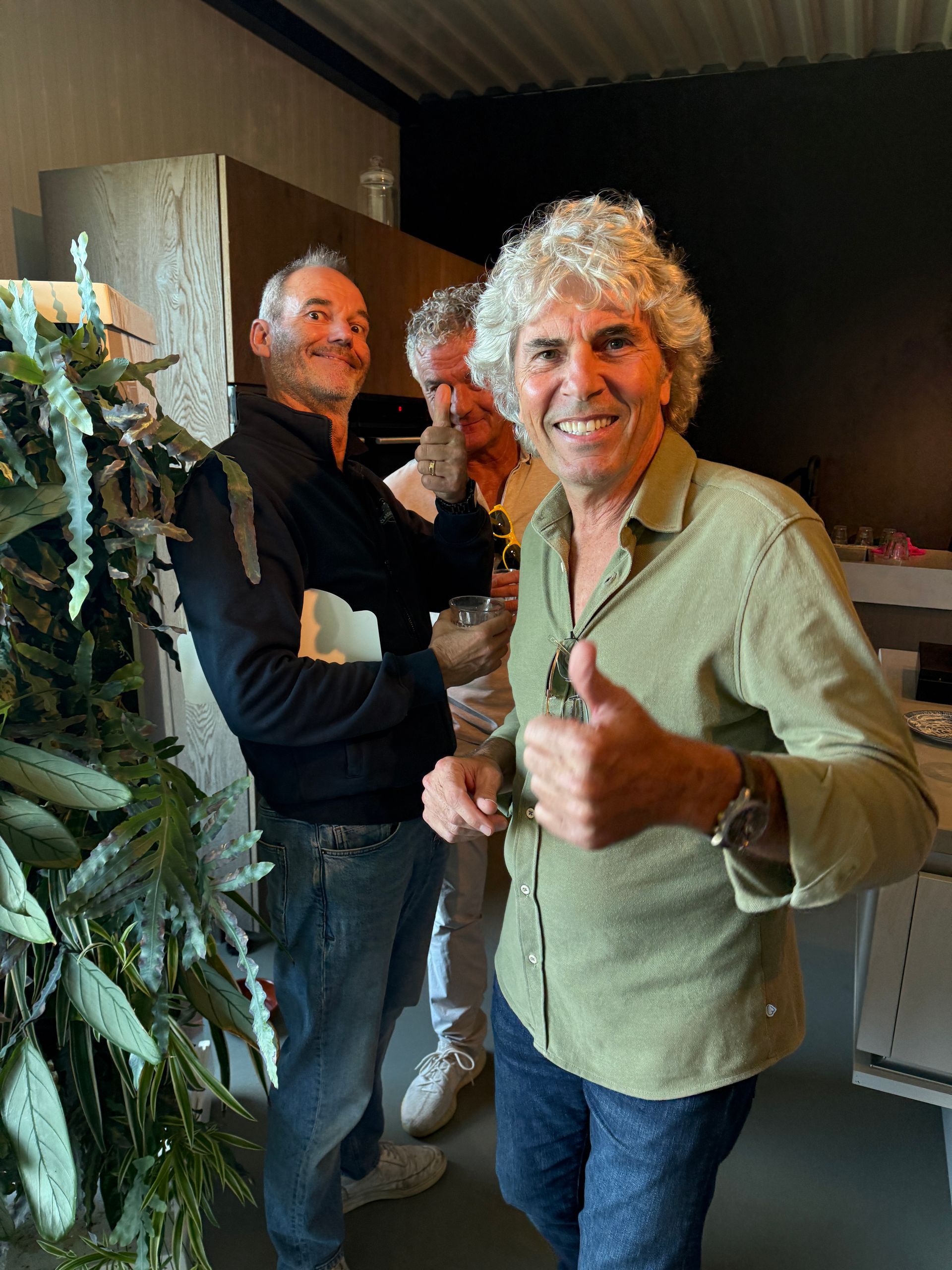 Drie mannen binnen; een van hen steekt zijn duim omhoog. Links hangt een feestelijke slinger.