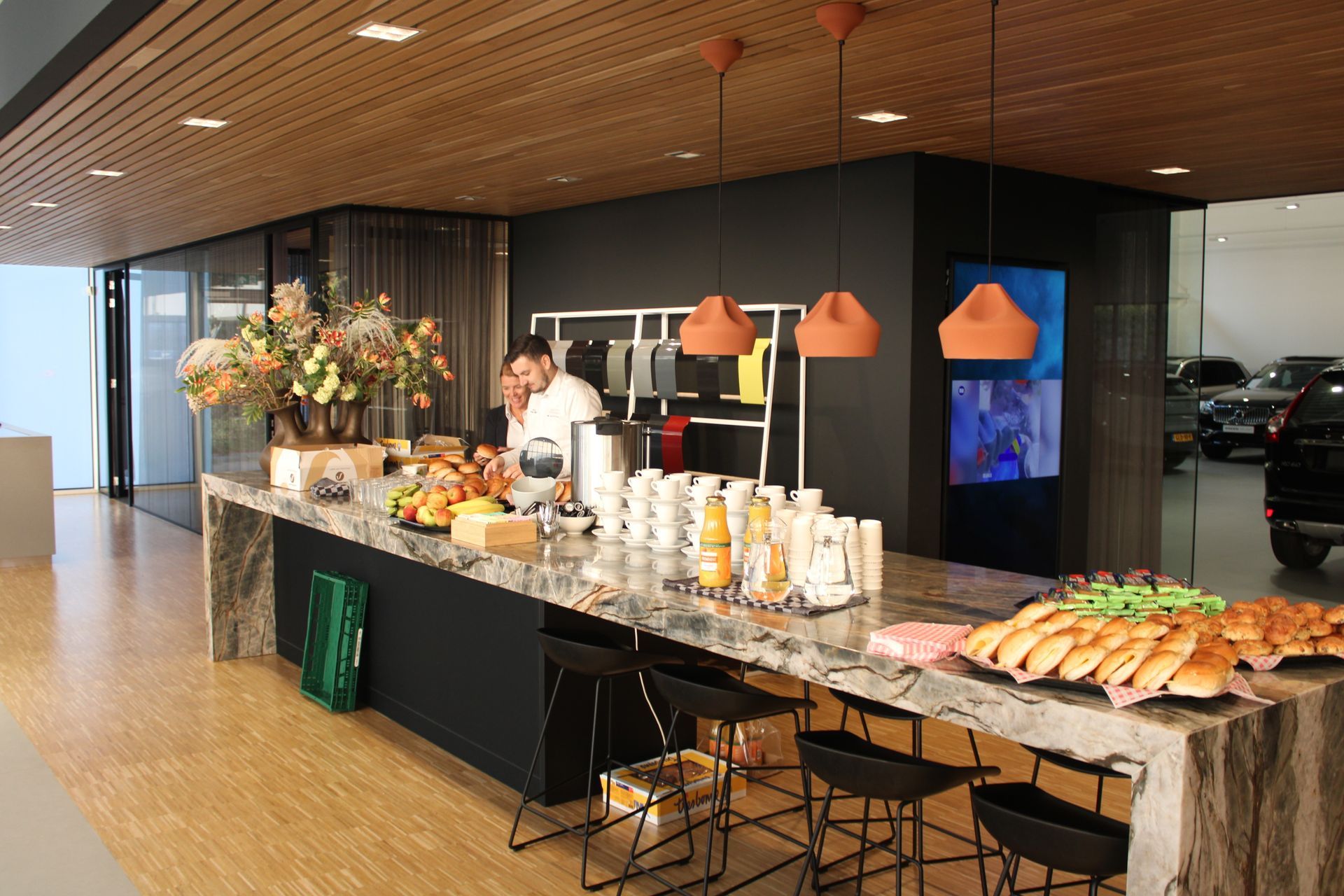 Een modern showroomcafé met een marmeren aanrechtblad, gebak en een medewerker achter de toonbank.