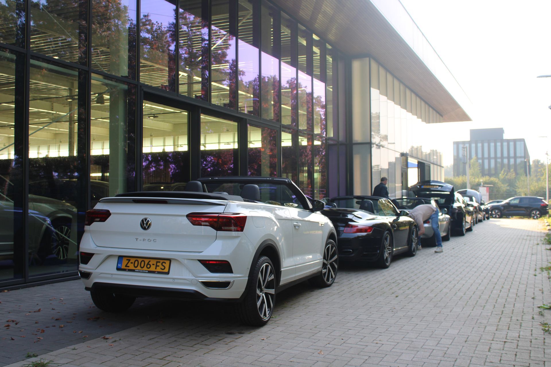 Een witte cabriolet-SUV staat geparkeerd voor een gebouw; andere auto's staan ​​langs de stoep opgesteld.