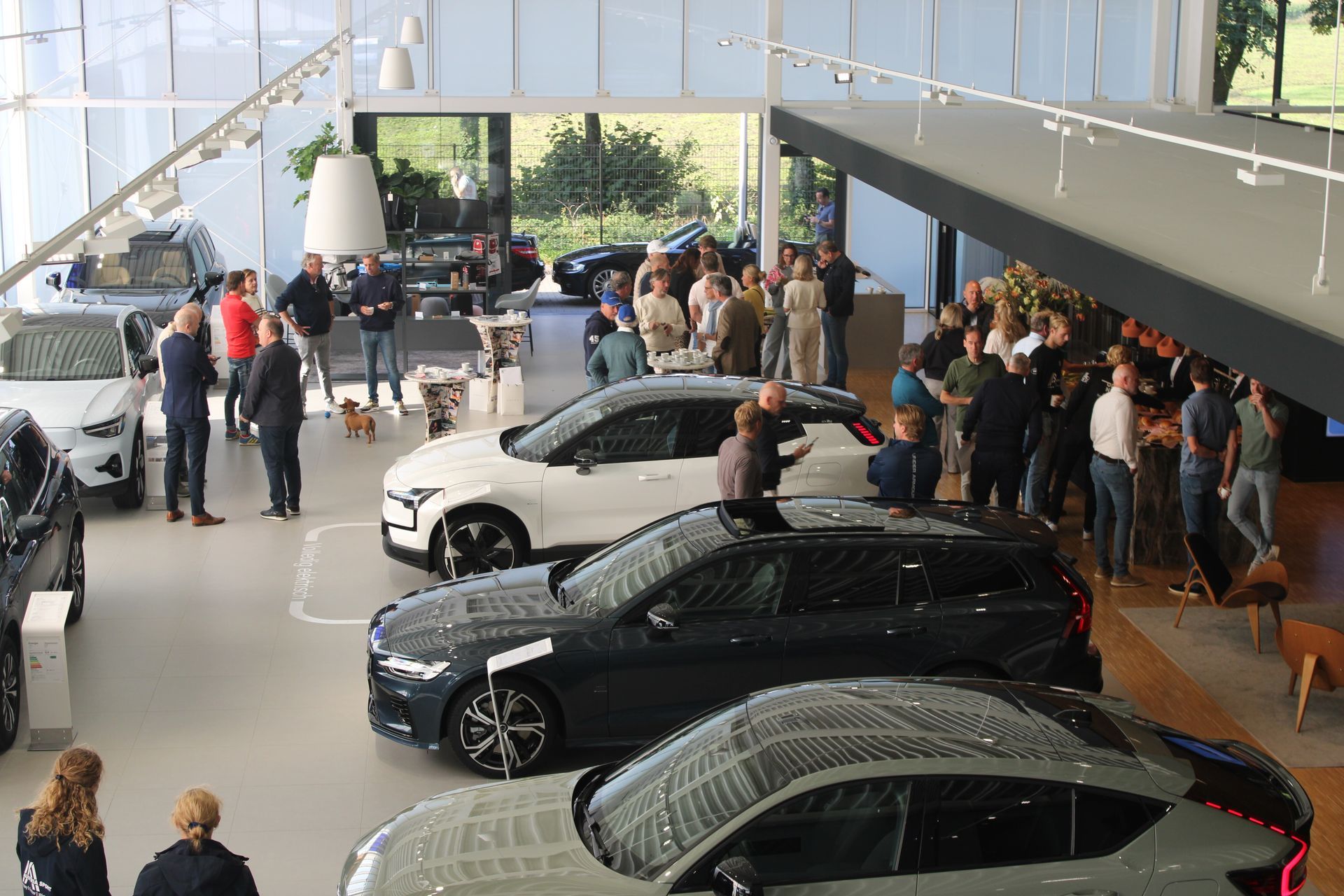 Mensen verzamelden zich in een autoshowroom om nieuwe auto's te bekijken. De auto's zijn zwart, wit en grijs.