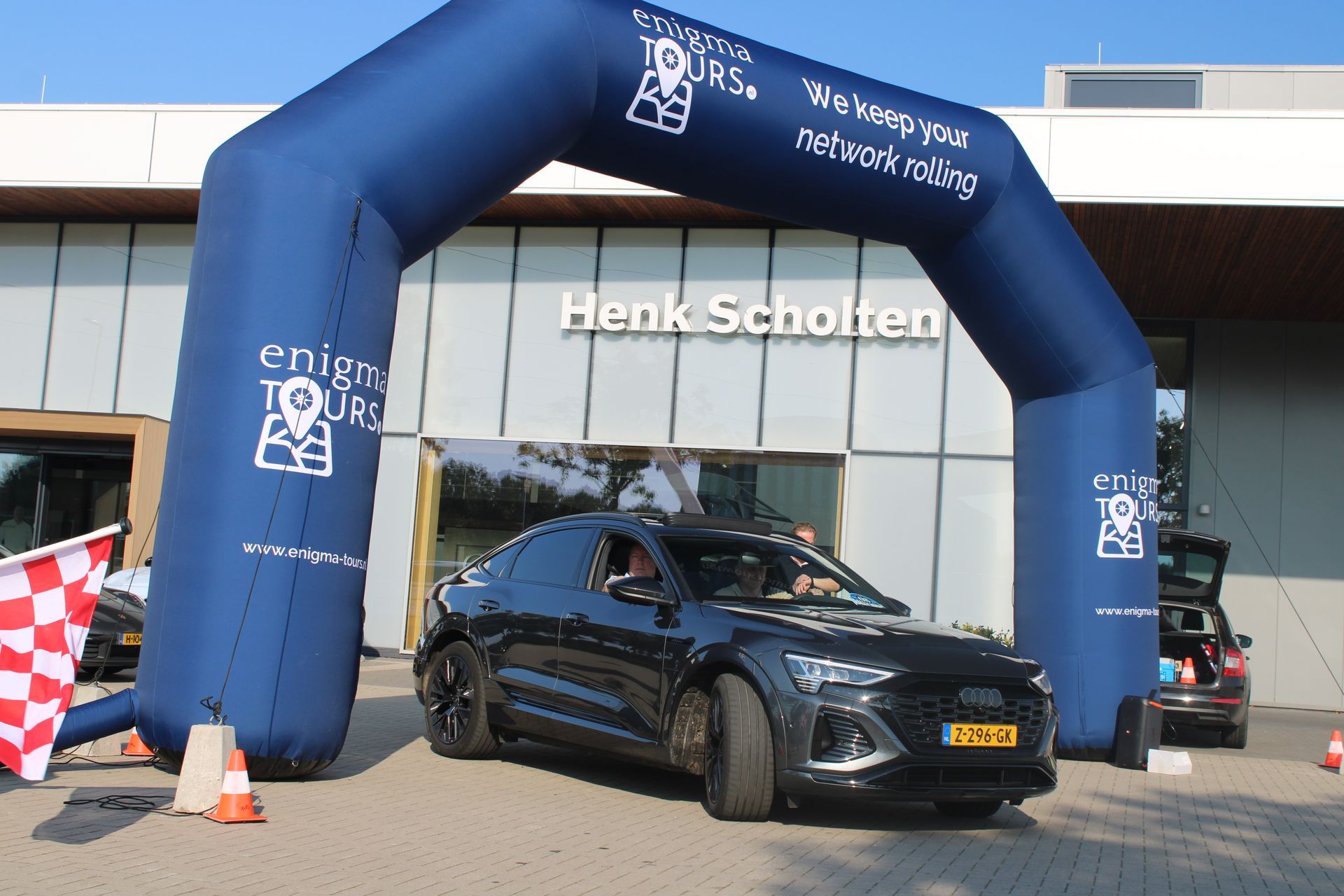 Een donkere auto rijdt onder een opblaasbare boog met het opschrift 