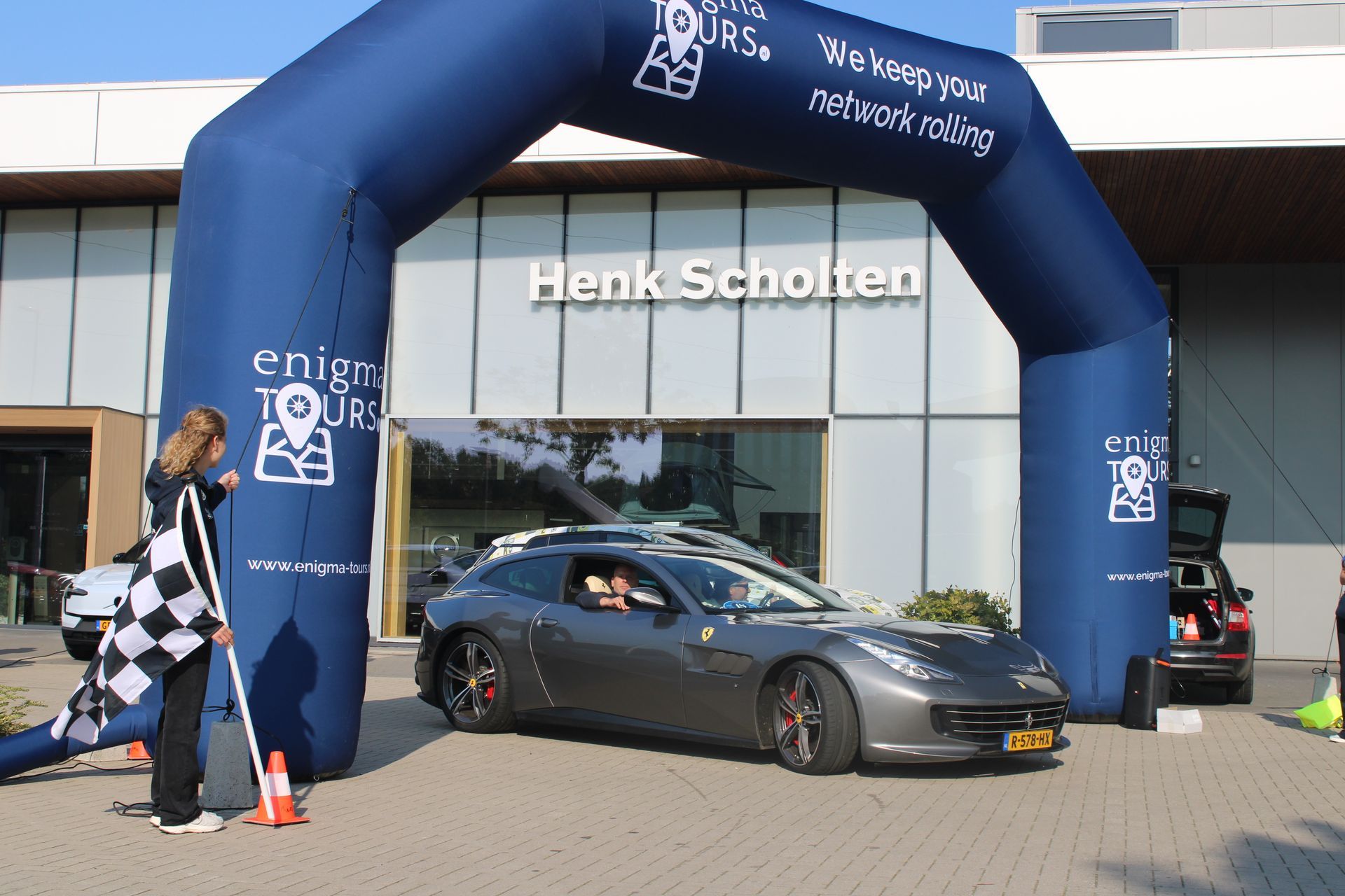Een grijze Ferrari rijdt onder een blauwe boog door met de naam 