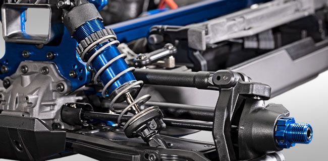 Close-up van een blauw-zilveren schokdemper en veersysteem op een voertuig, waarschijnlijk een modelauto.