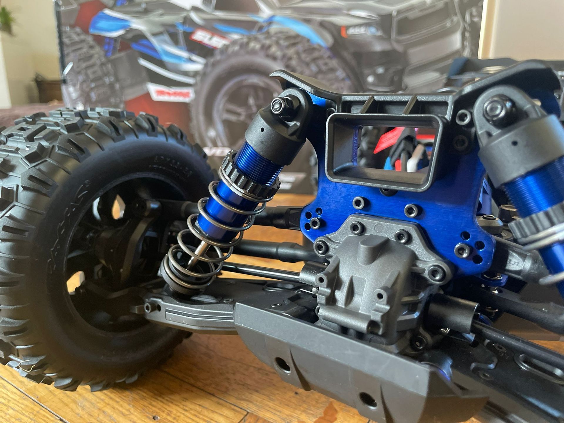 Blauw en zwart RC-truckchassis met schokdempers en banden, doos op de achtergrond.