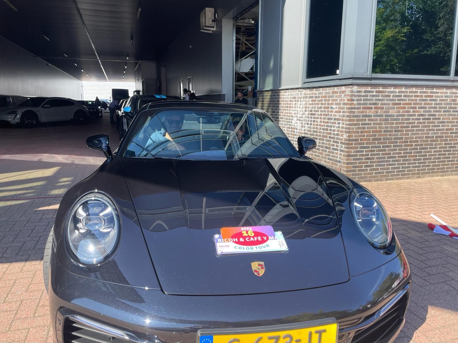 Donkergrijze Porsche 911 met een Europees kenteken staat geparkeerd voor een gebouw.