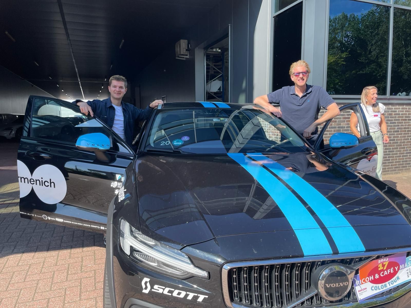 Twee mannen en een vrouw staan ​​buiten bij een zwarte auto met blauwe accenten.