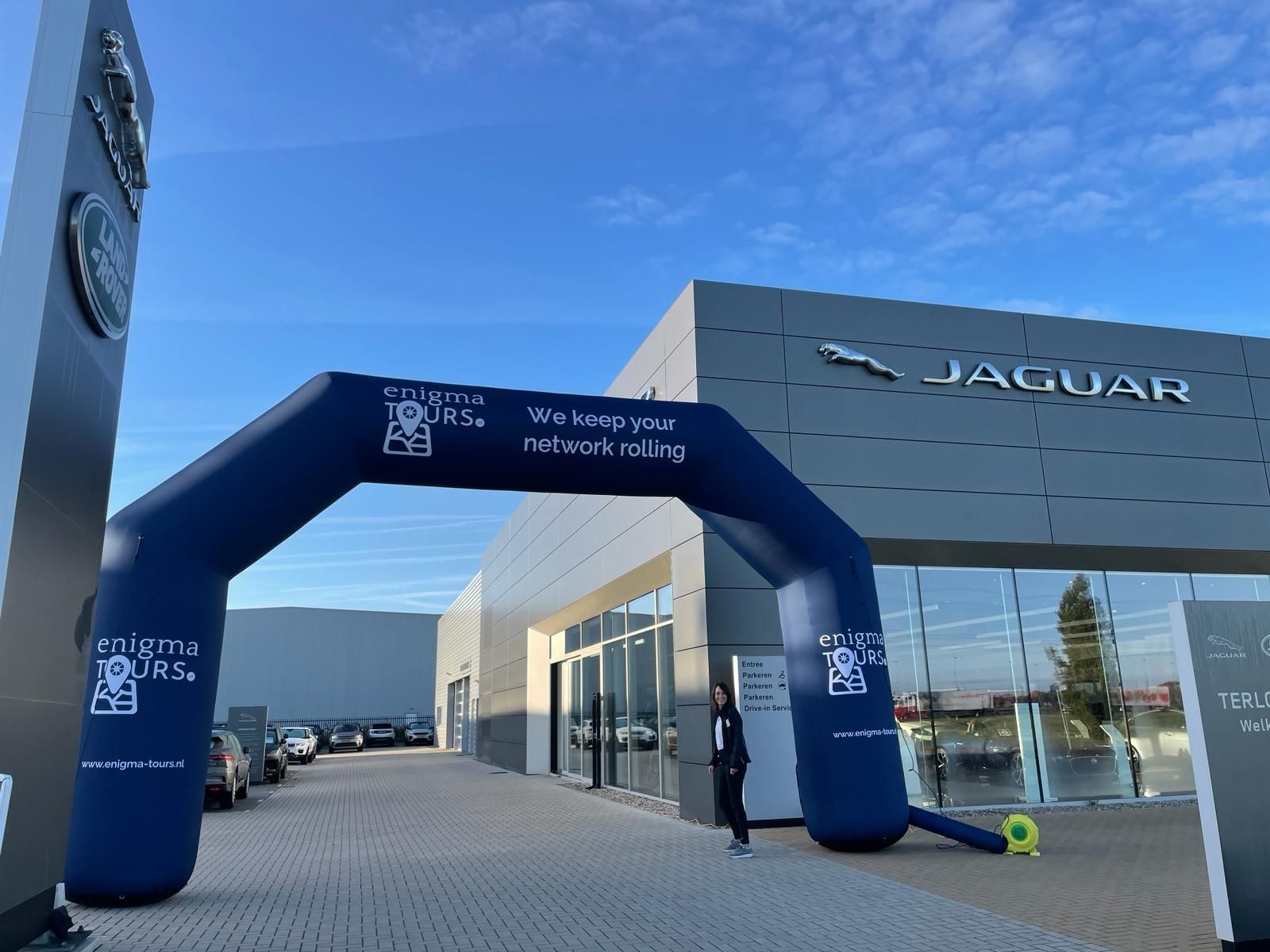 Blauwe opblaasbare boog bij de ingang van een Jaguar-dealer. Een persoon staat er vlakbij.