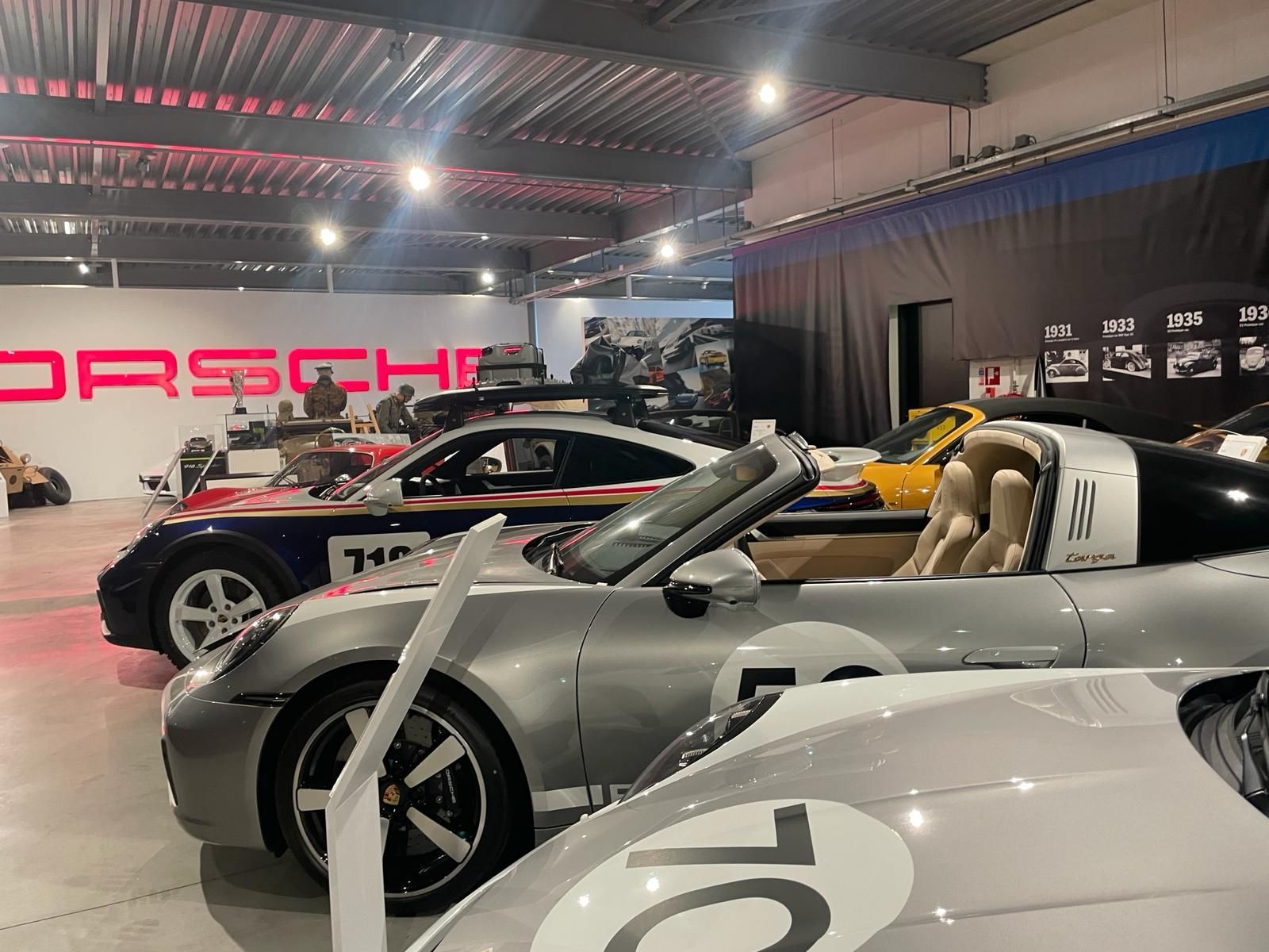 Een rij klassieke Porsches in een showroom, in zilverkleur met racestrepen. Het 