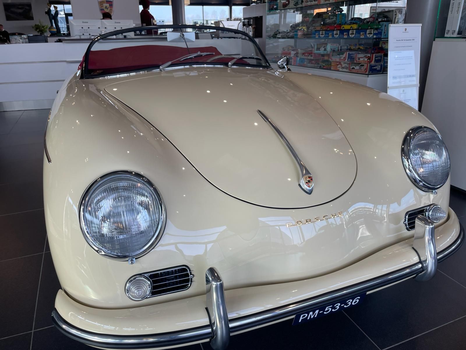 Crèmekleurige Porsche 356 cabriolet met chroomaccenten tentoongesteld in een showroom.