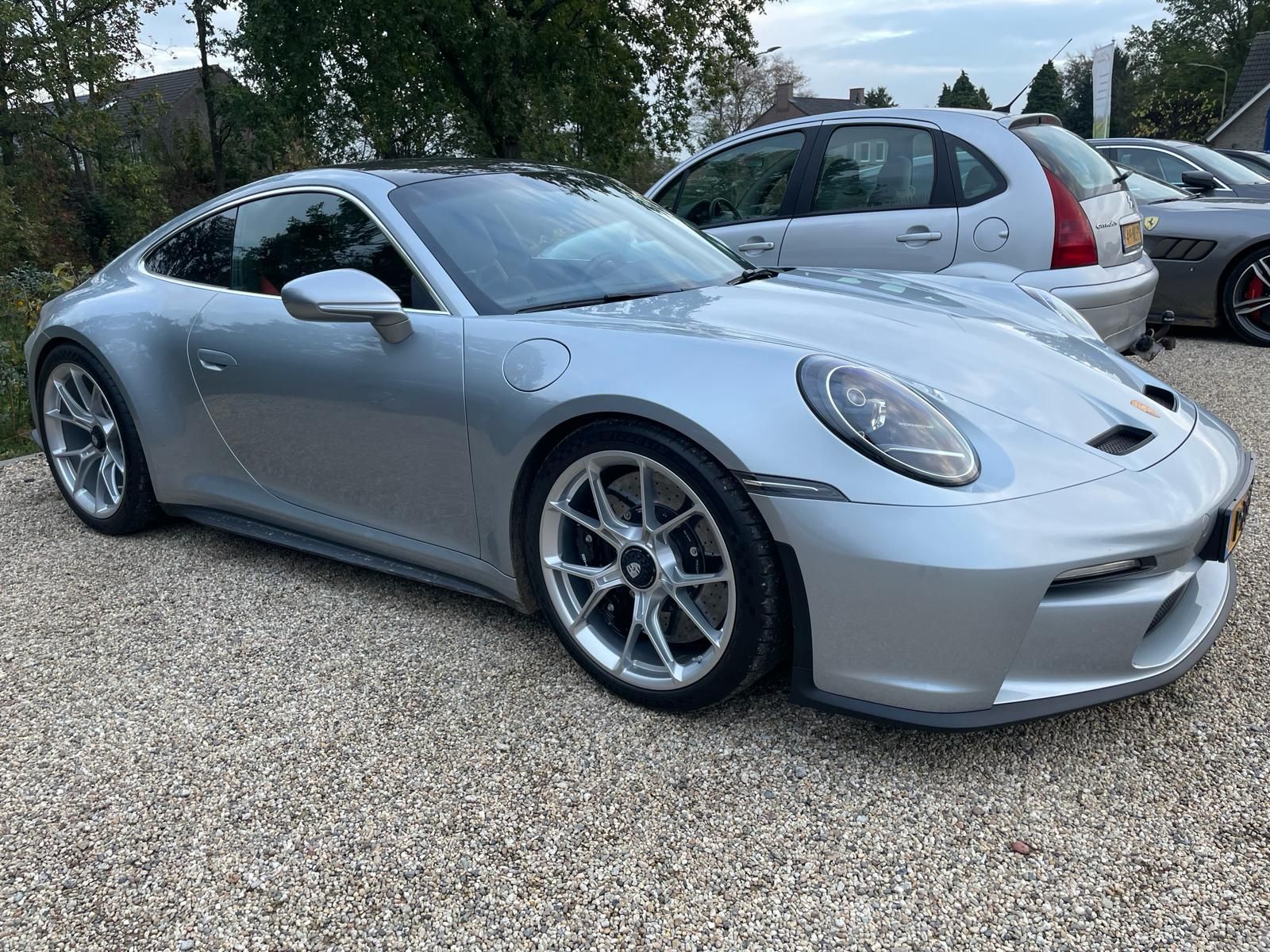 Een zilverkleurige Porsche sportwagen staat geparkeerd op een grindpad.