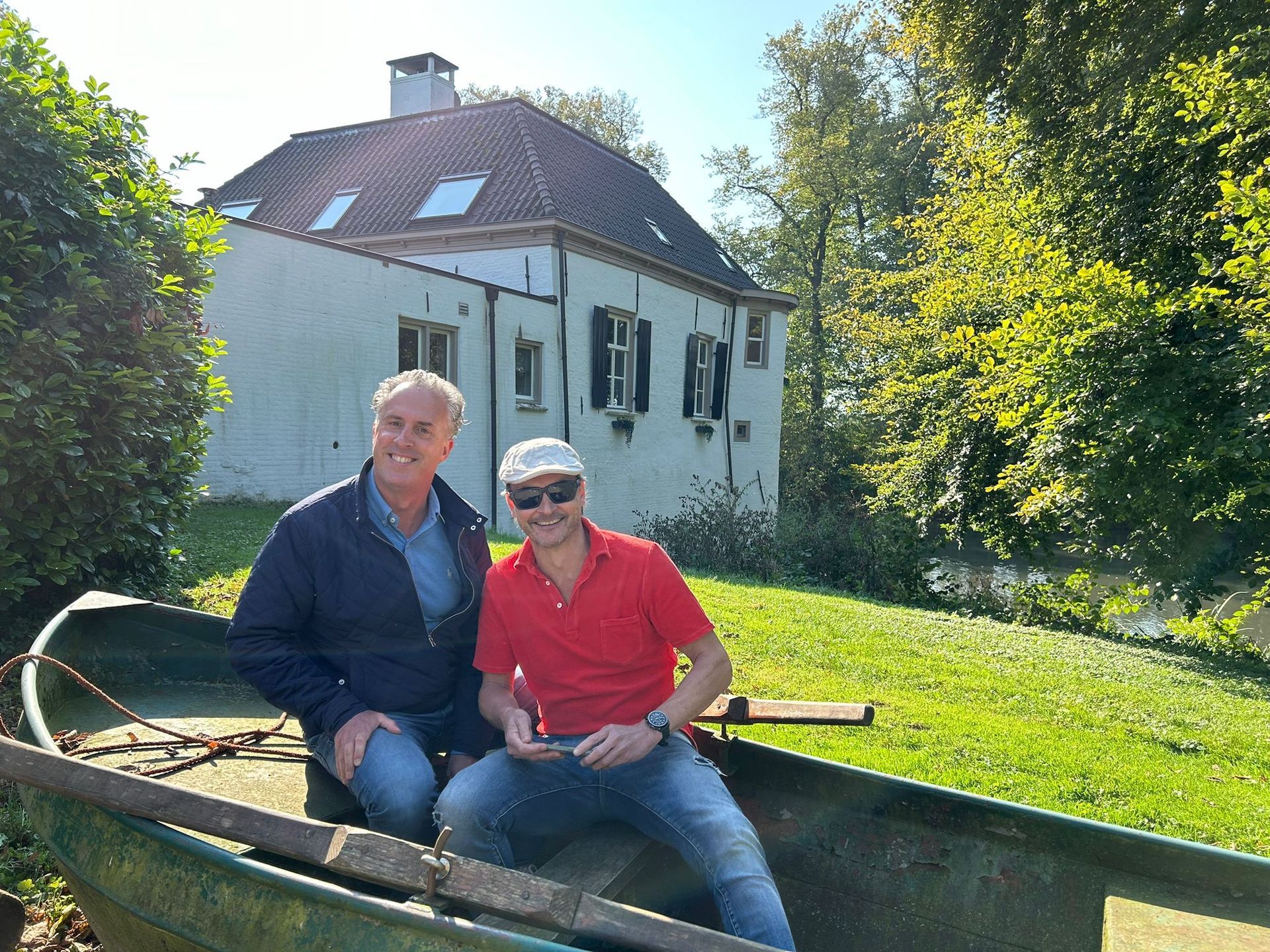 Twee mannen in een boot voor een wit gebouw met een groen gazon. Zonnige dag.