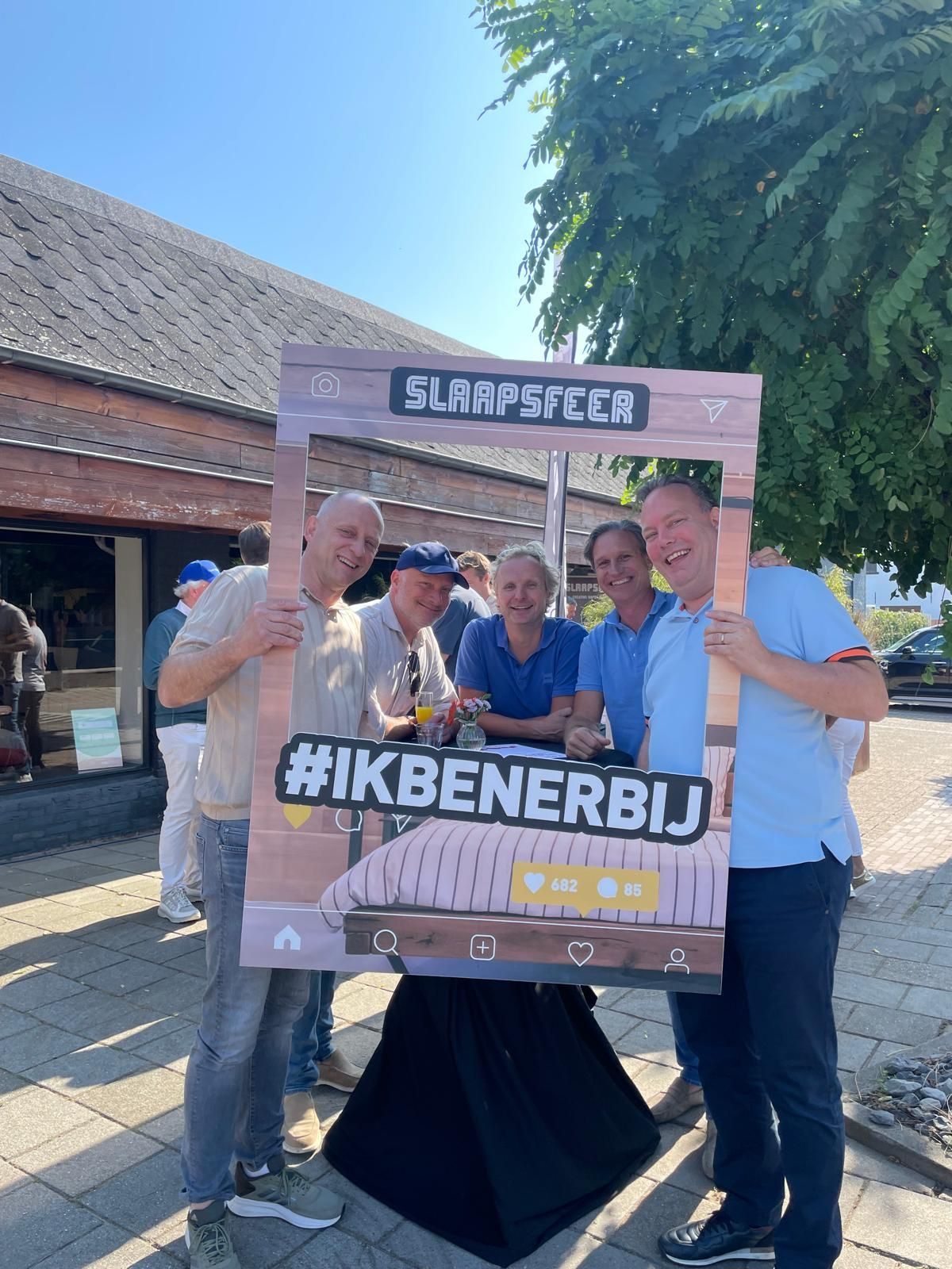 Vijf lachende mensen, die een fotolijstje vasthouden met de tekst