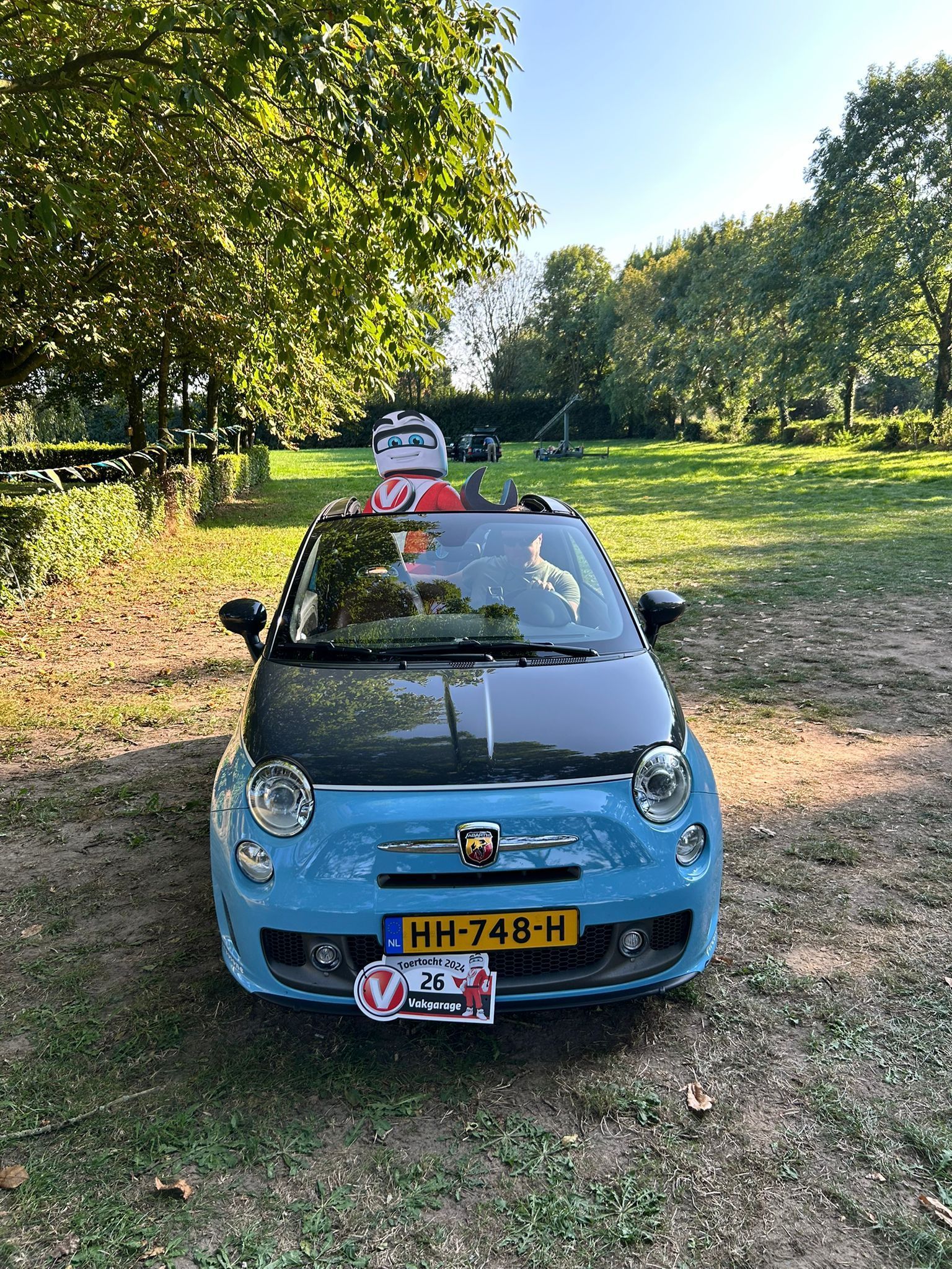 Een lichtblauwe Fiat 500 met een carbonfiber motorkap, geparkeerd op een grasveld met een zichtbaar Lego-figuurtje.