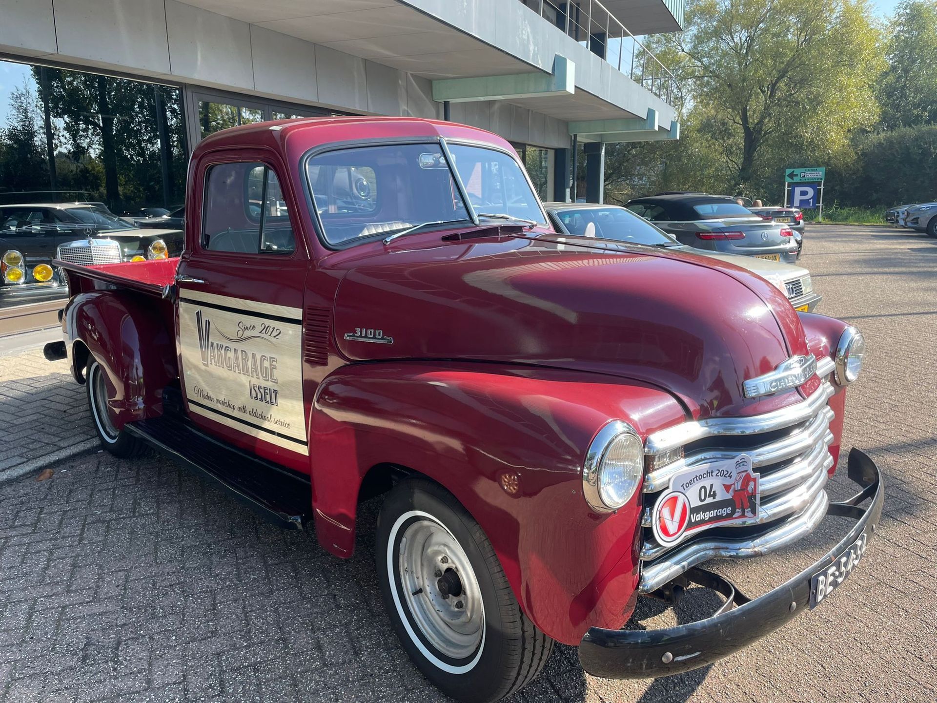 Een klassieke bordeauxrode Chevrolet pick-up truck staat geparkeerd voor een gebouw.