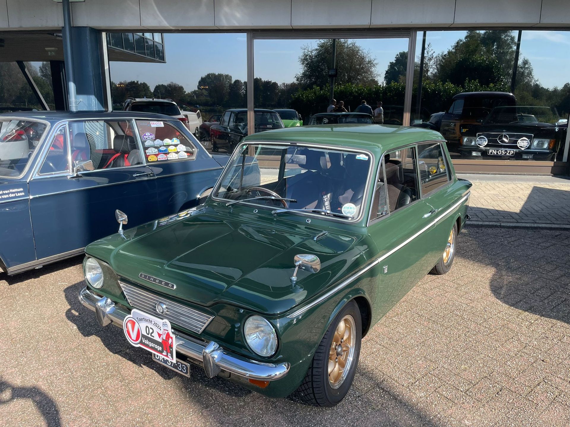 Groene oldtimer geparkeerd op grind, met andere voertuigen erachter zichtbaar.
