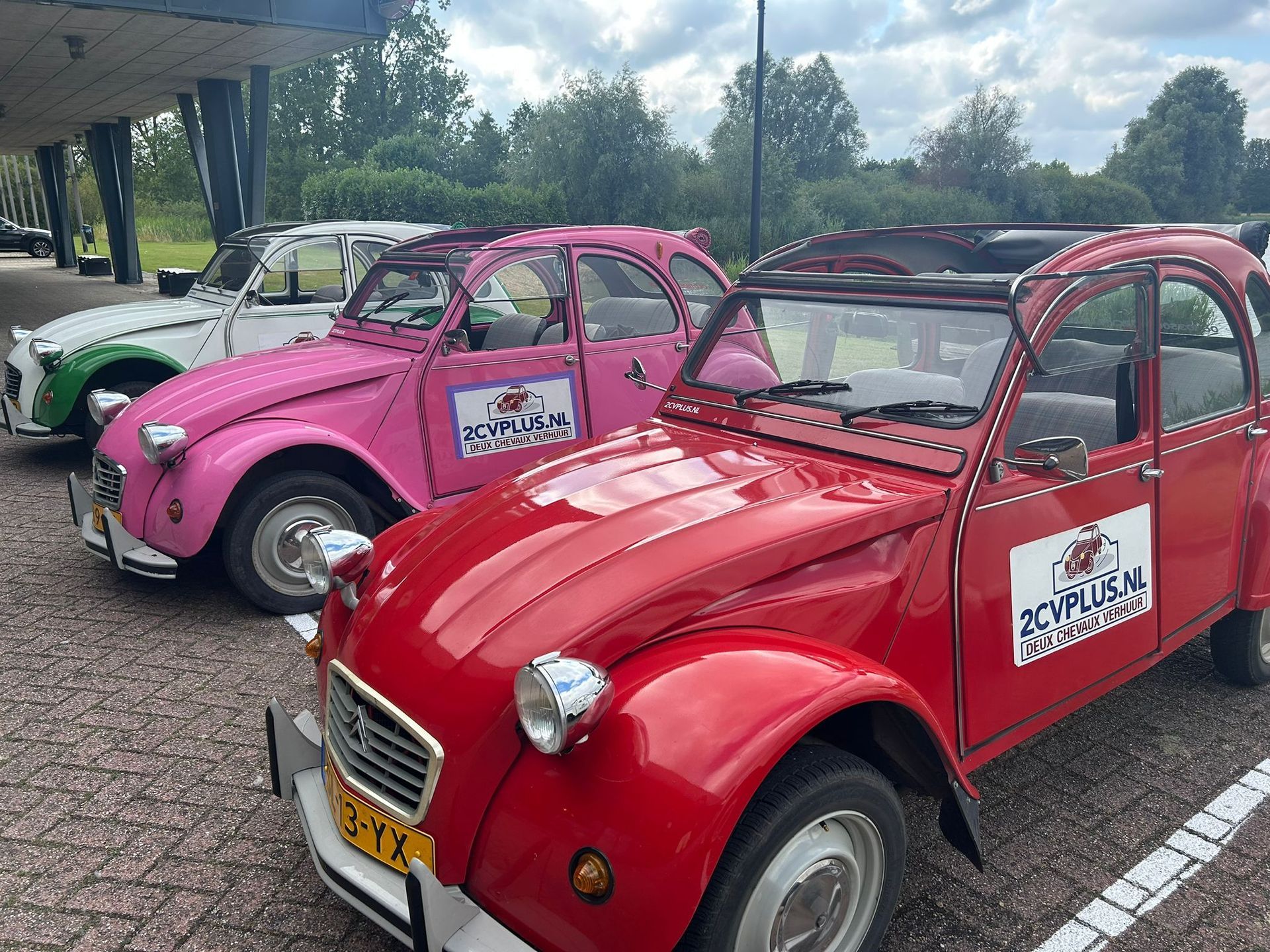 Drie oldtimers, rood, roze en wit, staan ​​op een rij geparkeerd.